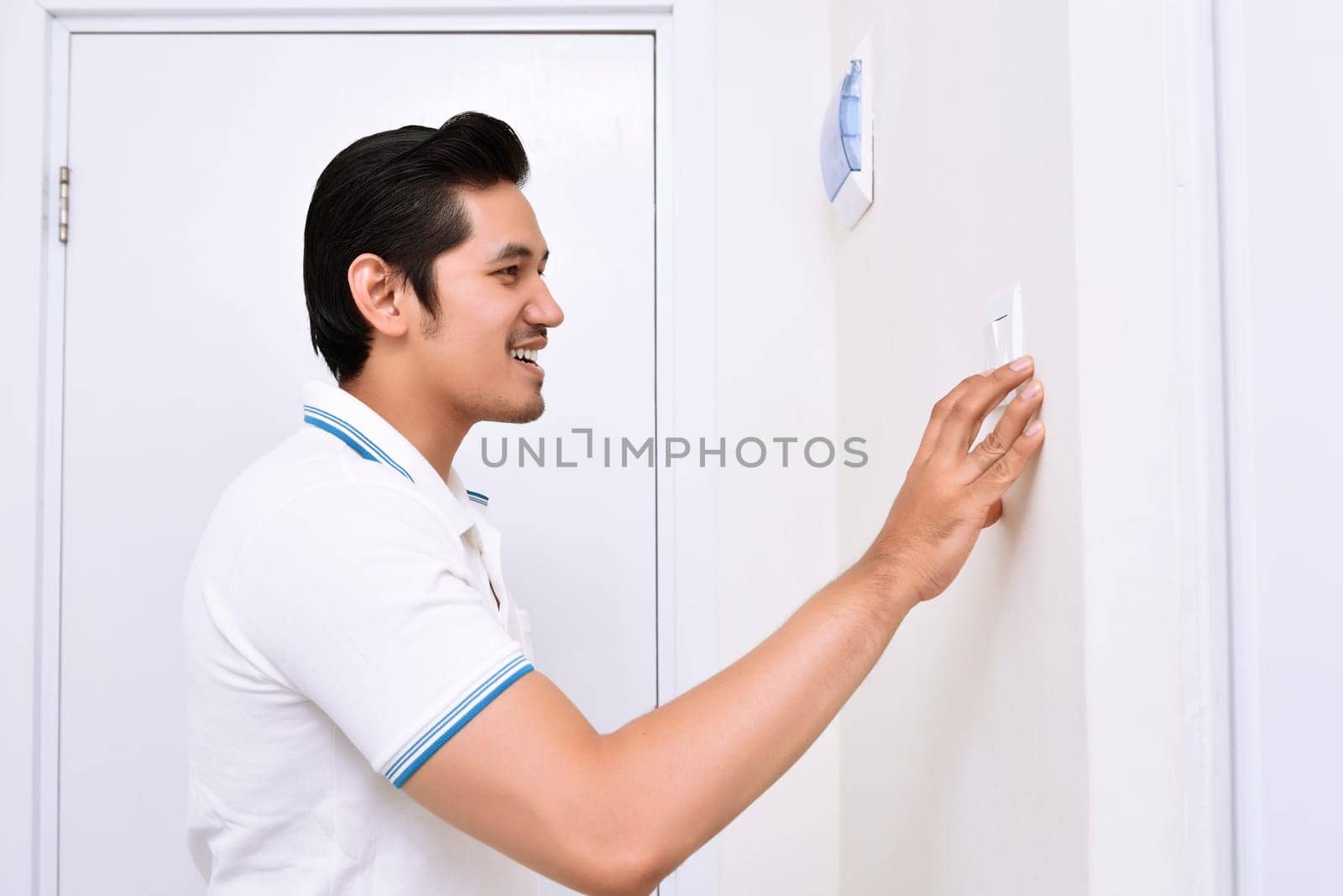 Handsome asian man turning off the light with wall switch in the home