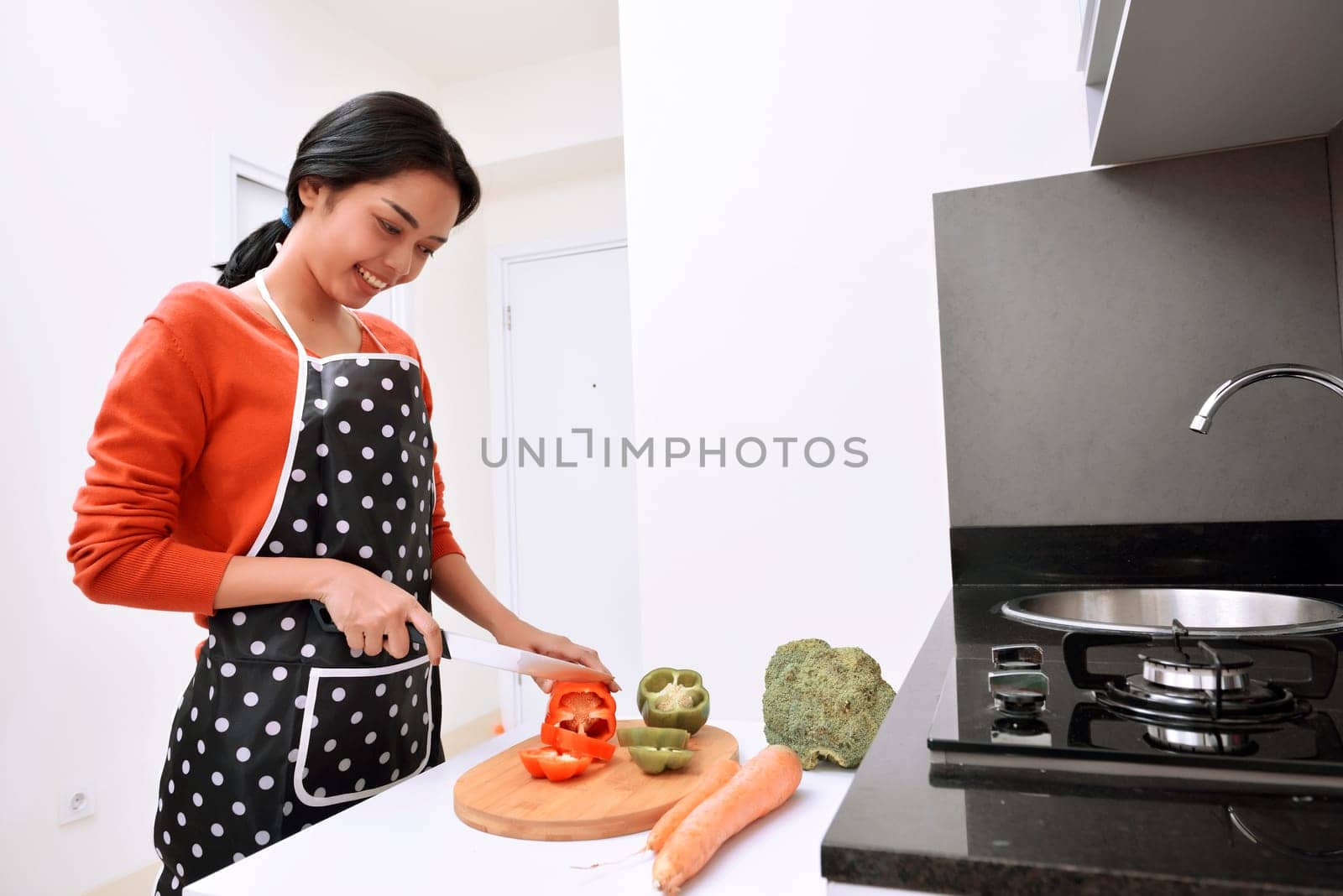 Smiling asian woman using knife to slice peppers and cooking in the kitchen