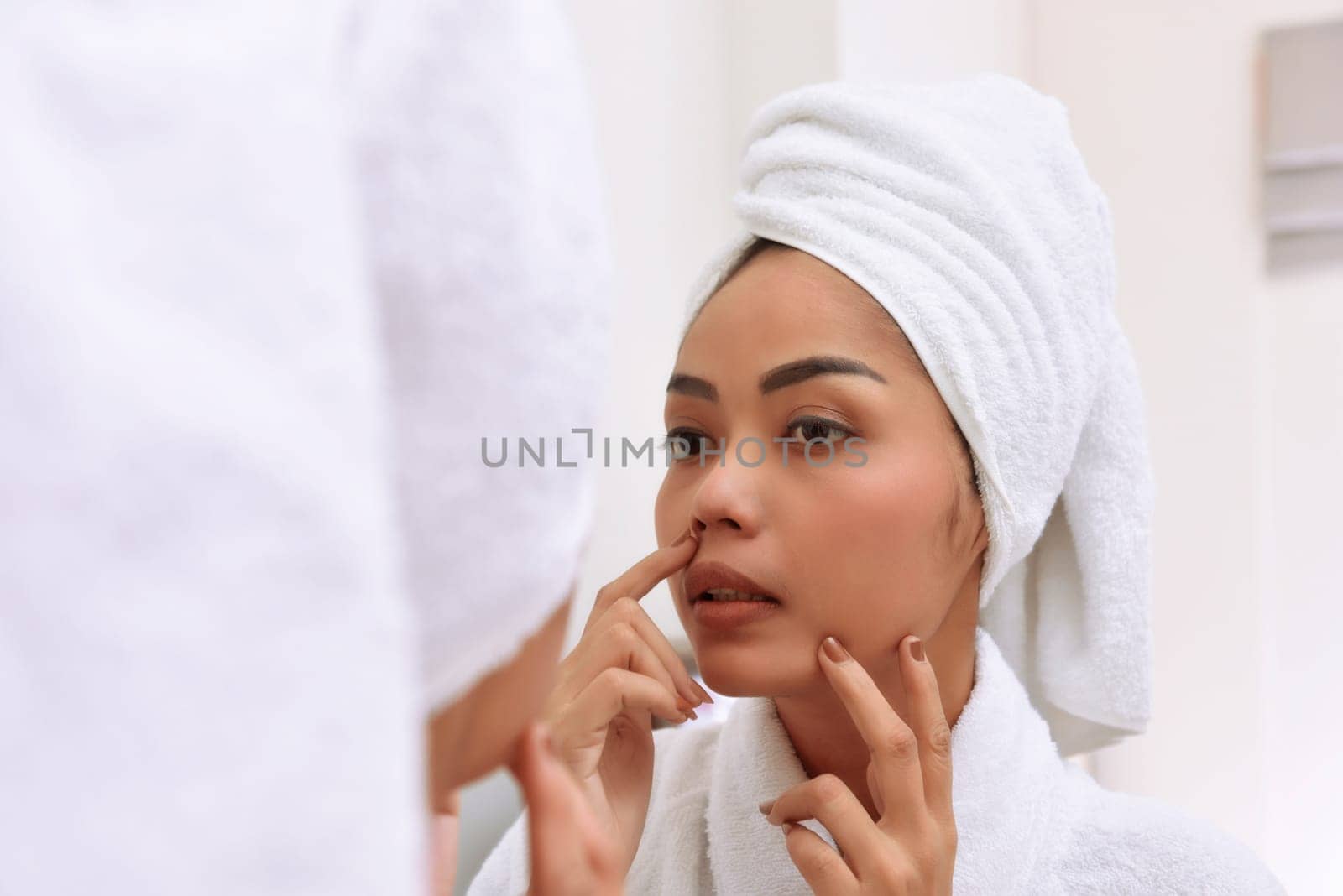 Young asian woman with bath towels cleanses her face at the bathroom
