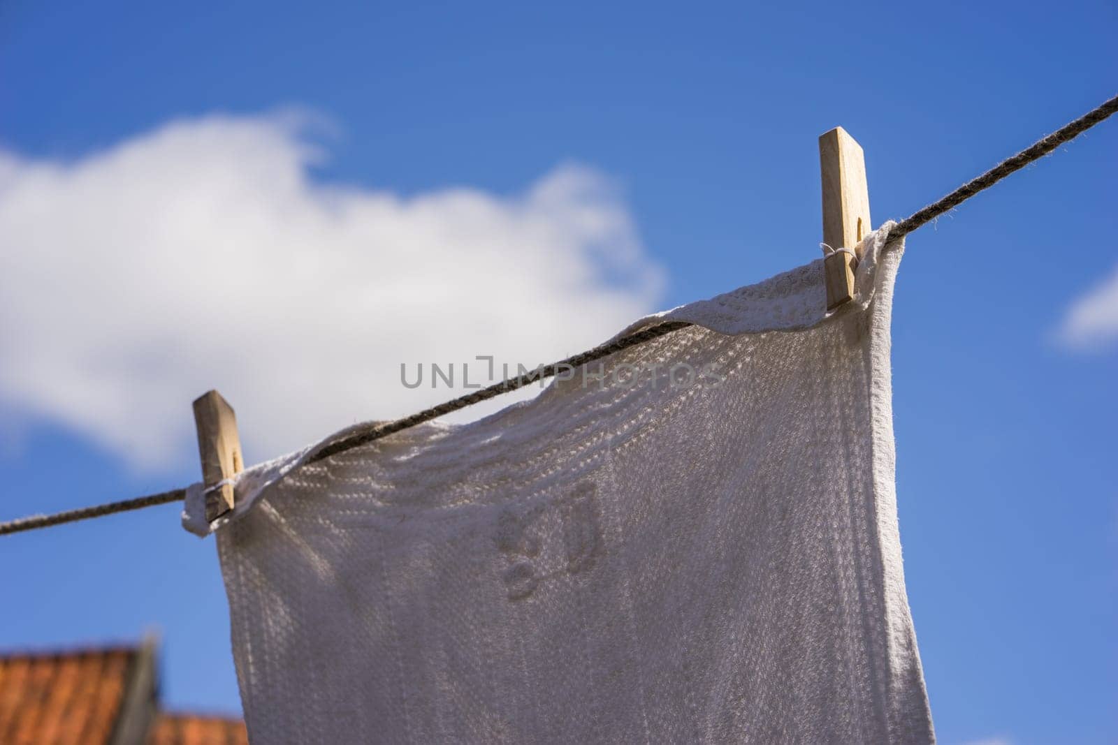 Closeup of white laundry hanging out against the blue sky with old-fashioned wooden clips