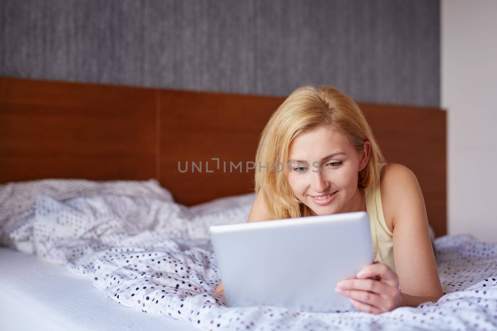 A beautiful young woman working on her tablet while lying on her stomach in bed