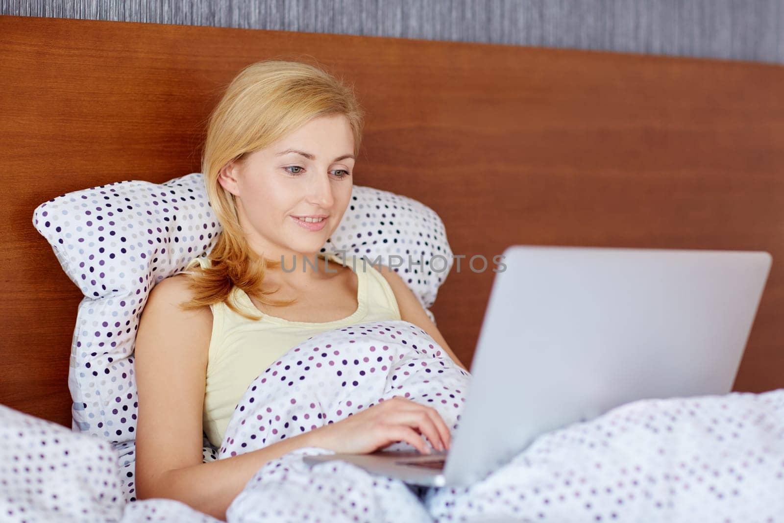 A young woman working on her laptop while lying in bed