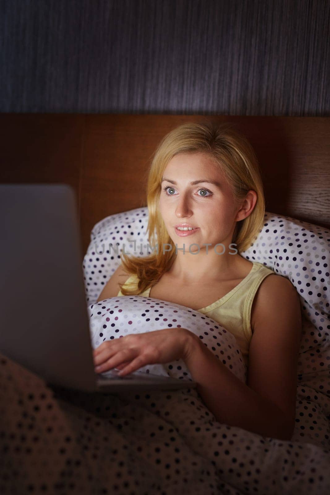 A young woman working on her laptop while lying in bed