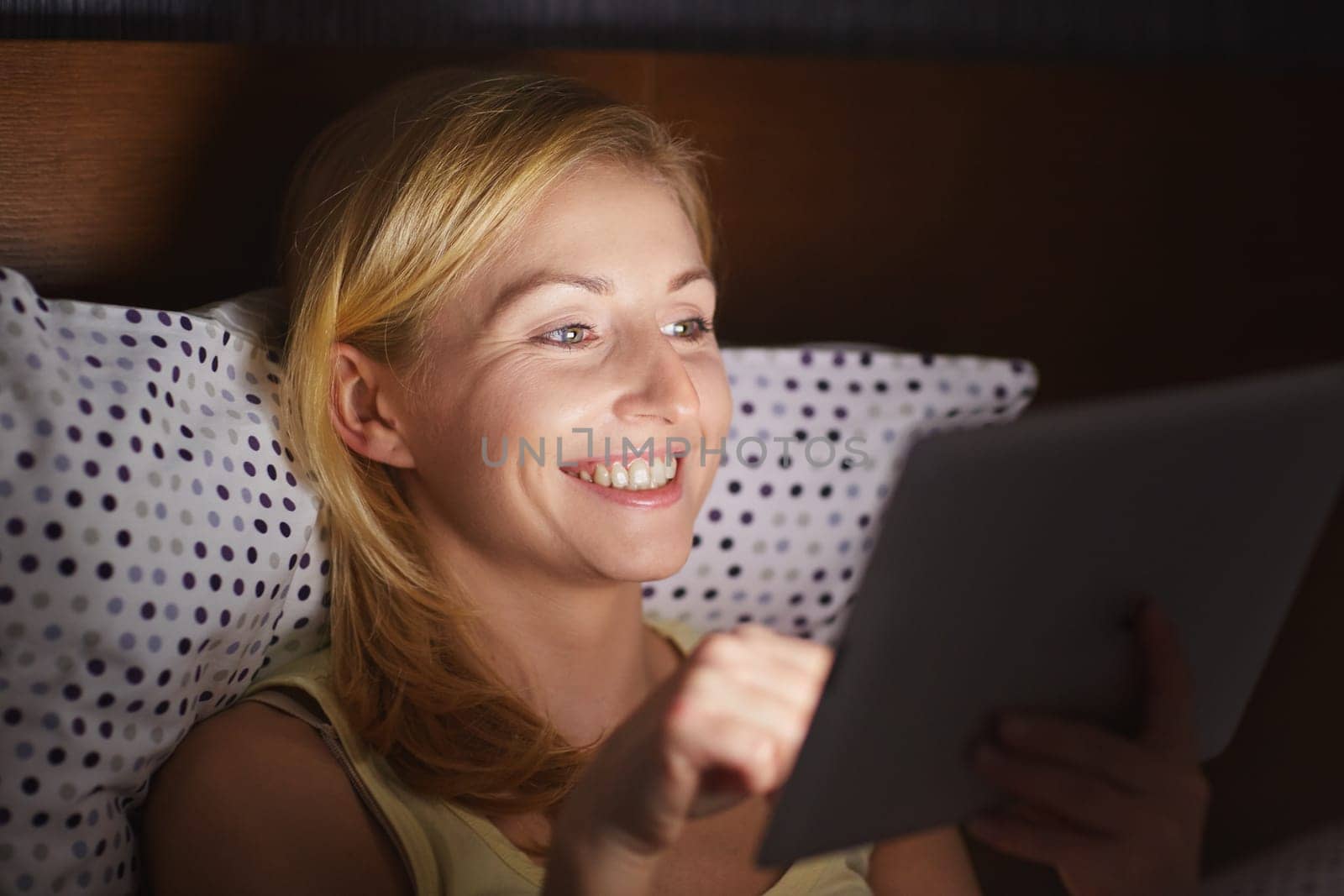 A young woman working on her tablet while lying in bed