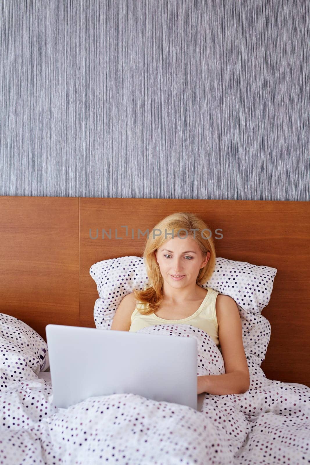 A young woman working on her laptop while lying in bed