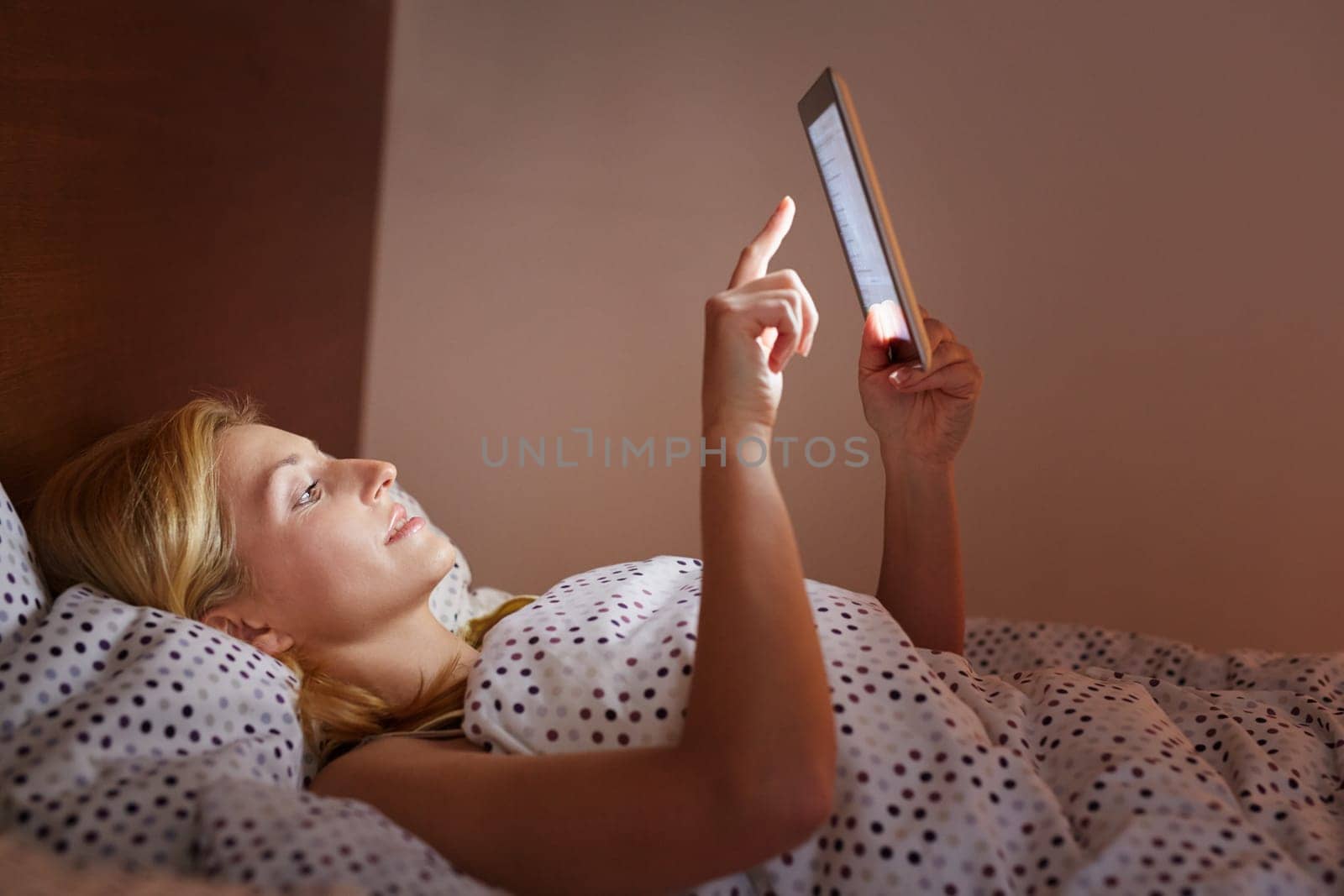 A young woman working on her tablet while lying in bed