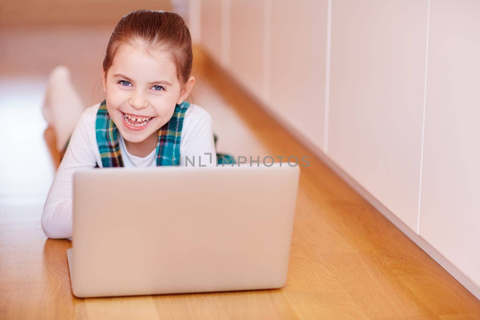 A cute little girl smiling at the camera while playing on a laptop