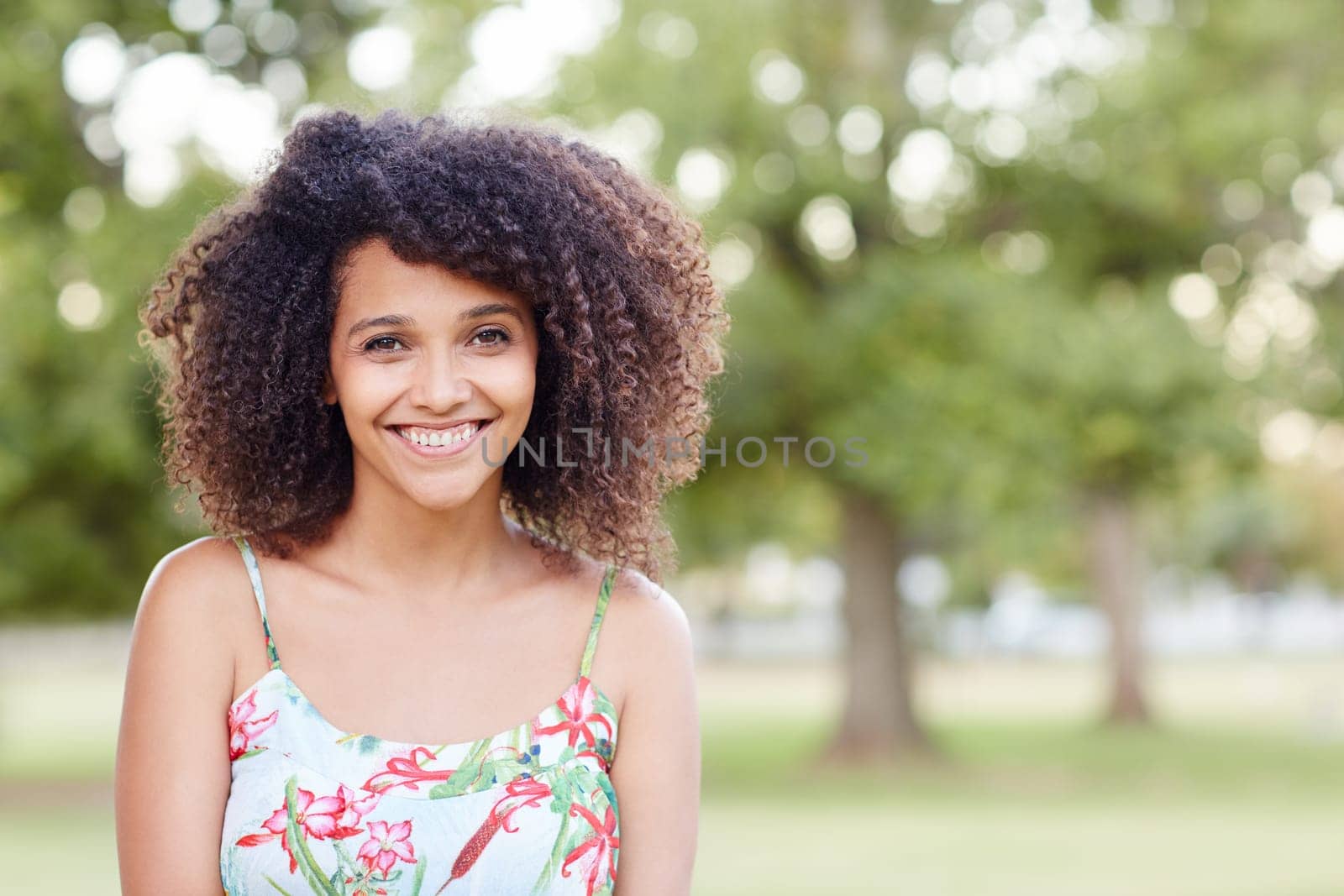 A young woman standing a park with trees behind her