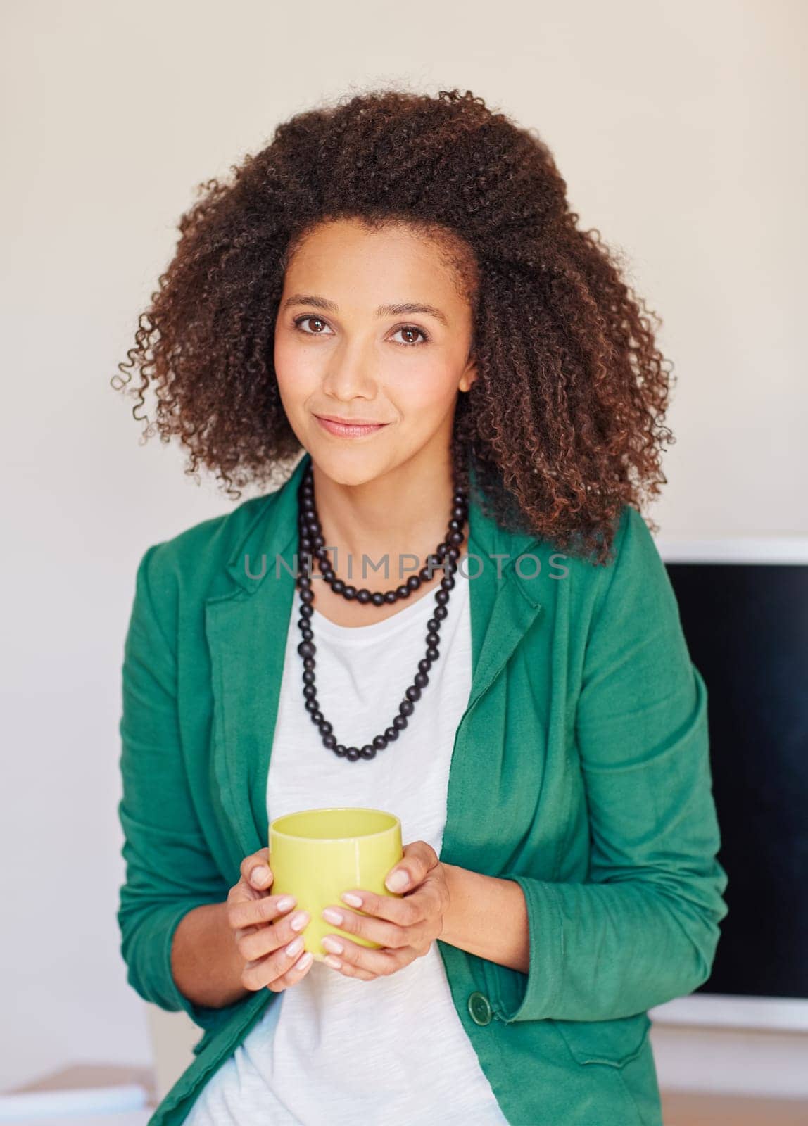 A young businesswoman holding a coffee cup while leaning against her desk