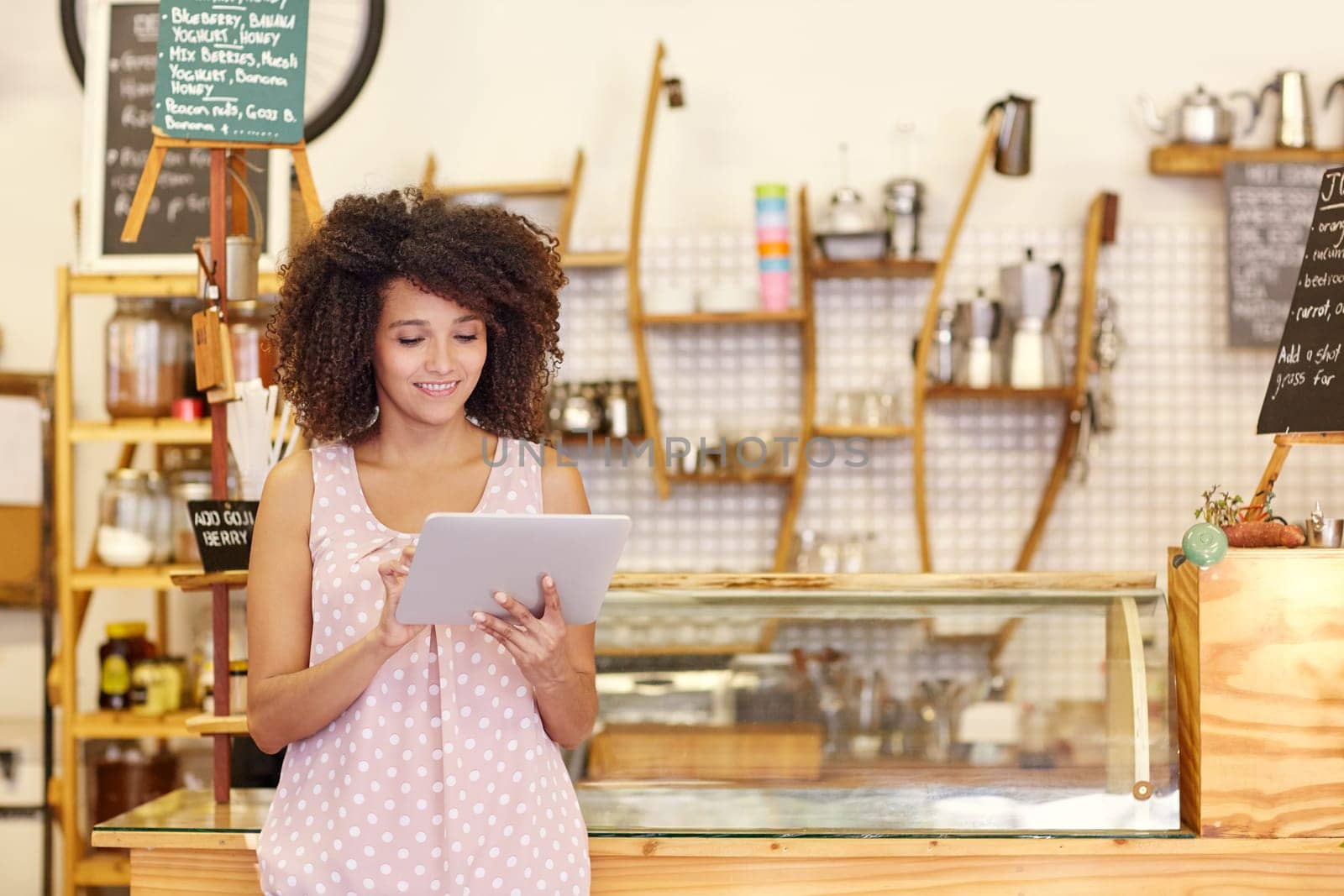 Beautiful cafe owner running her small business with the help of a digital tablet while standing near the counter of her coffee shop