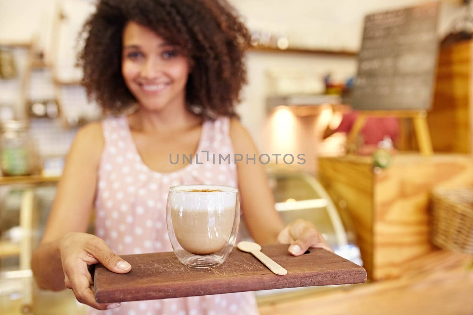 Focus on the foreground of a latte ay being carried on a wooden tray by a young mixed race waitress