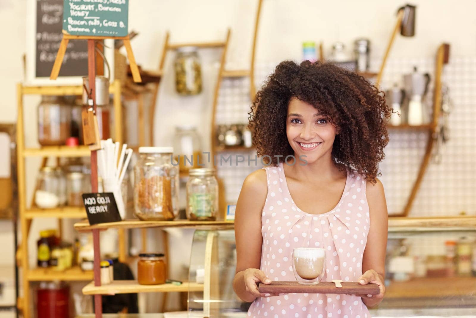 Beautiful young mixed race waitress carrying a latte in a modern glass mug on a wooden tray
