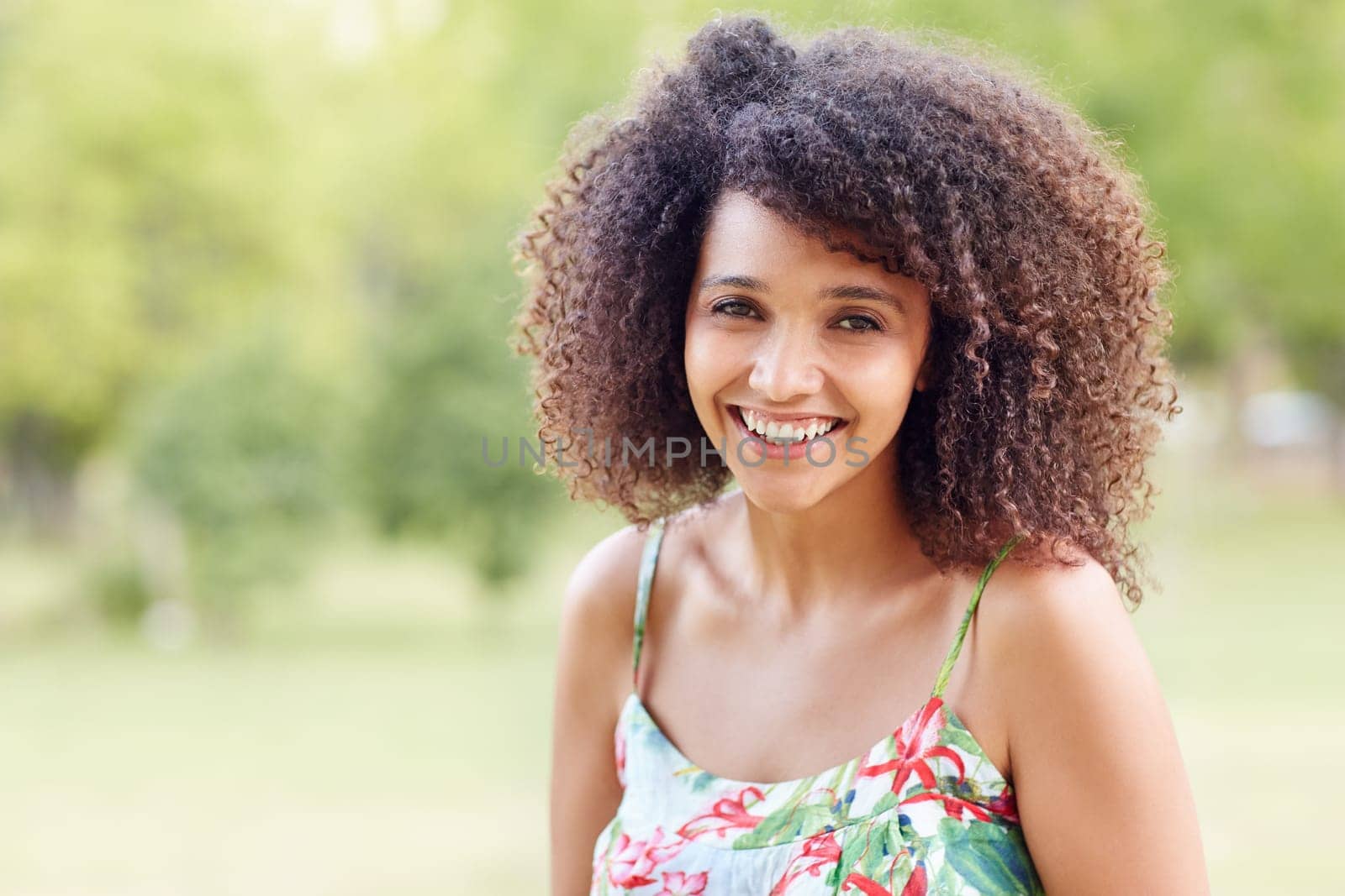 Young beautiful mixed race woman with curly afro hair smiling happily in a green park