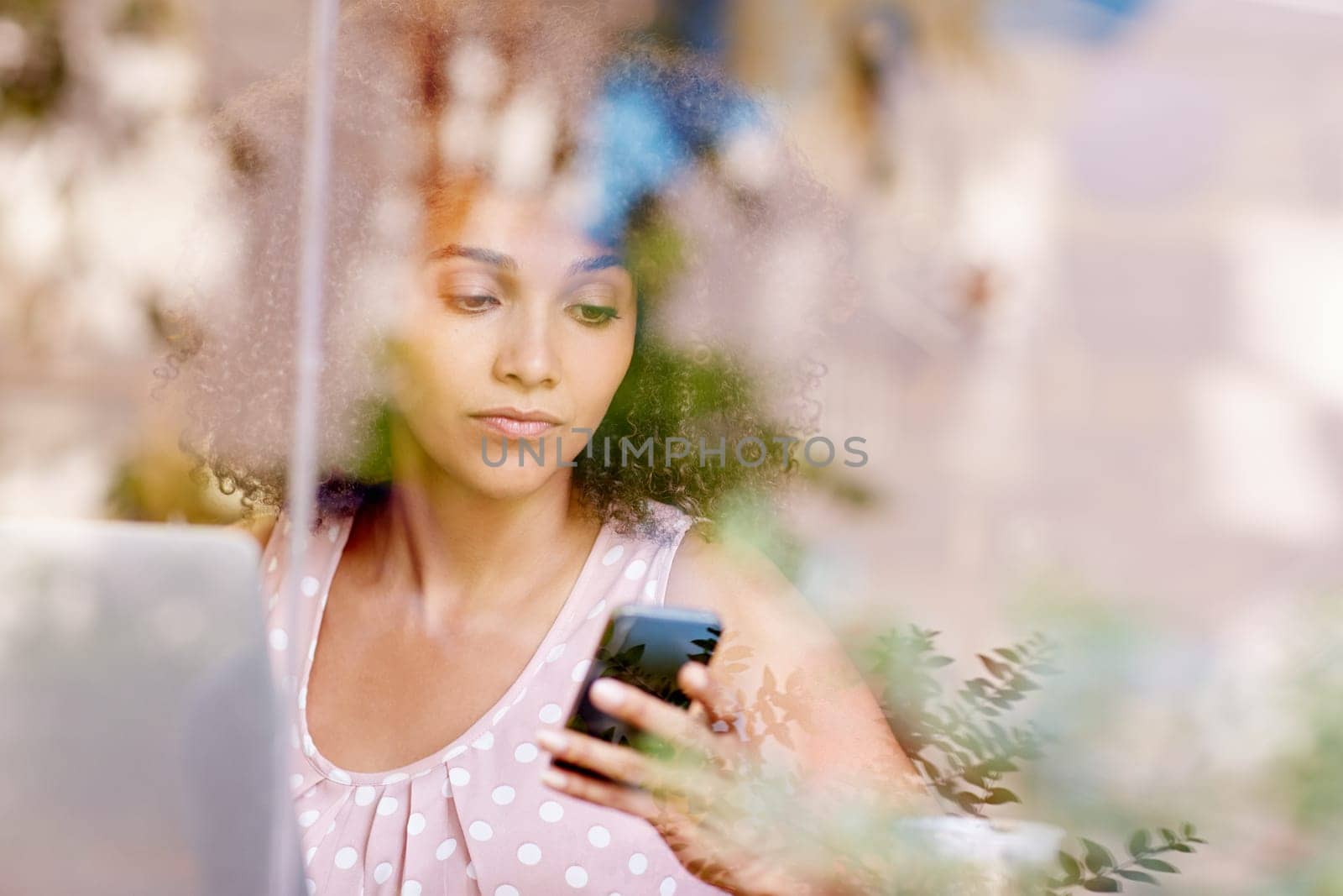 Beautiful mixed race woman sitting in a coffee shop, seen through the window while typing on her mobile phone