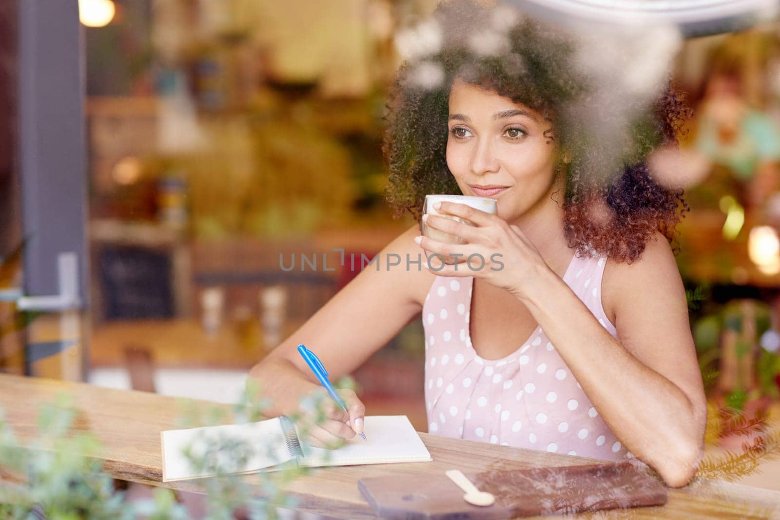 Beautiful mixed race woman sitting in a coffee shop sipping her latte and daydreaming while gazing out of the window