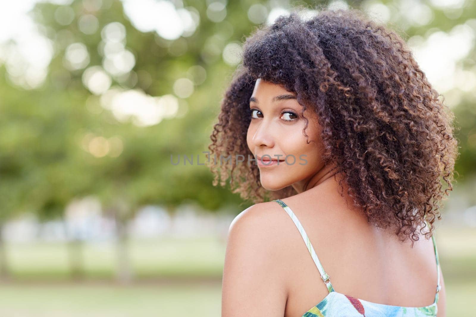 Portrait of a beautiful young woman in a park looking back over her shoulder at you
