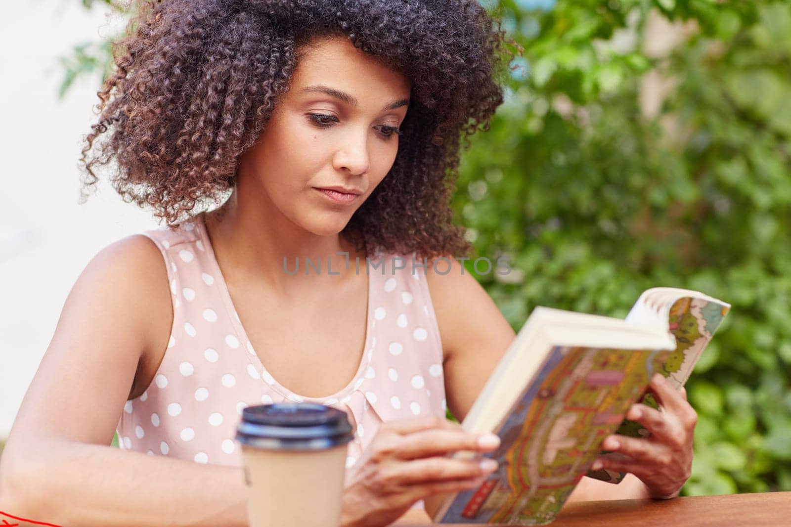 A young woman reading a book while drinking coffee outside