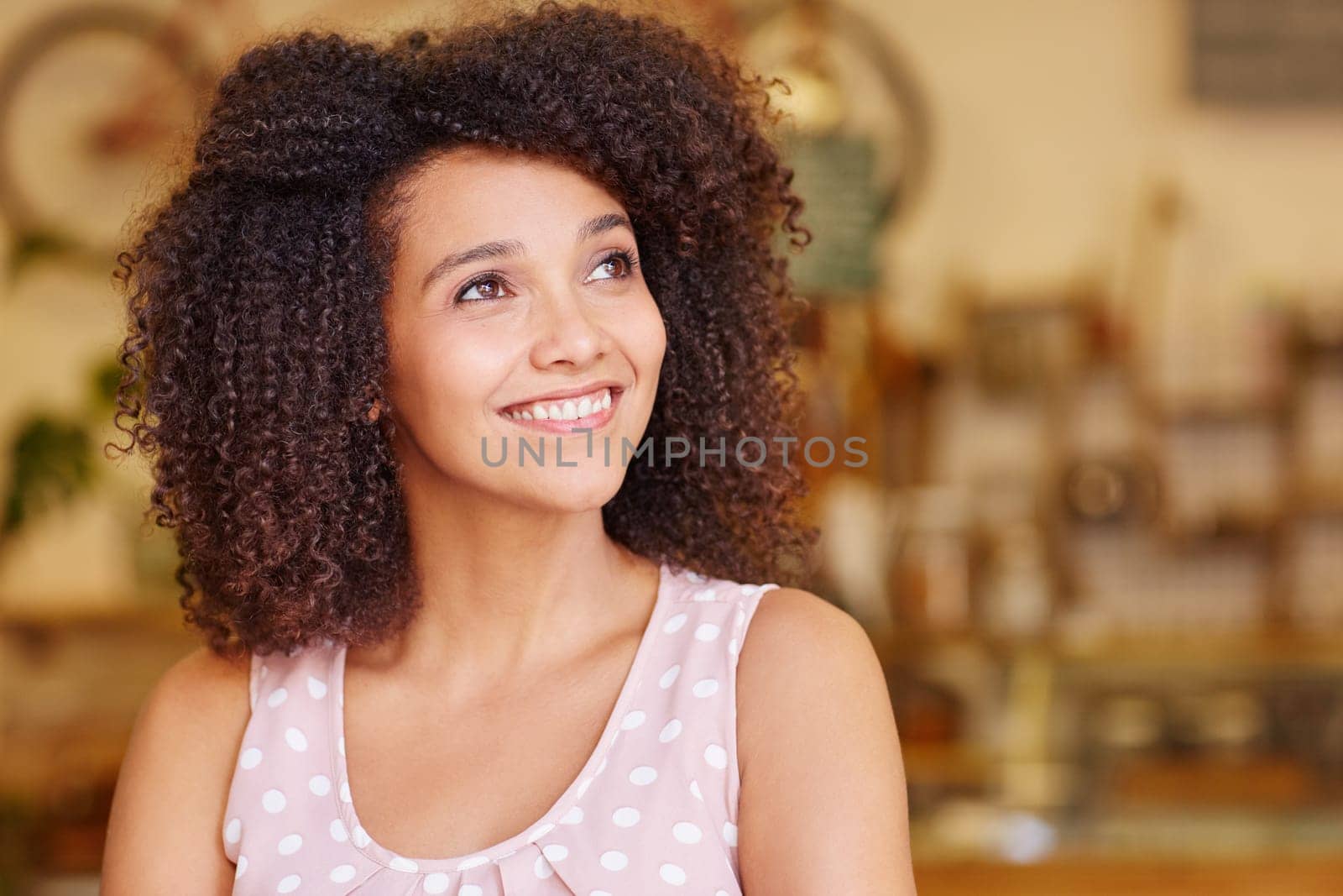 Beatiful young woman with gorgeous afro hair smiling and daydreaming in a coffee shop