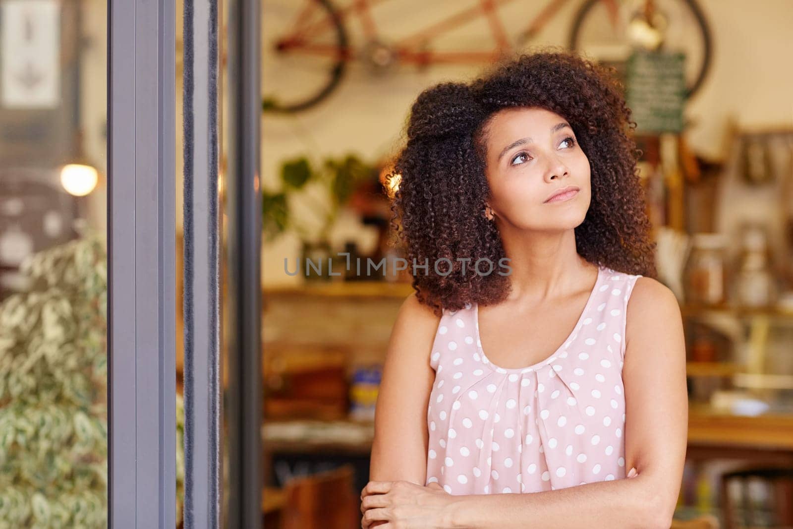 Beautiful young woman standing in the doorway of her coffee shop thinking about the future of her small business