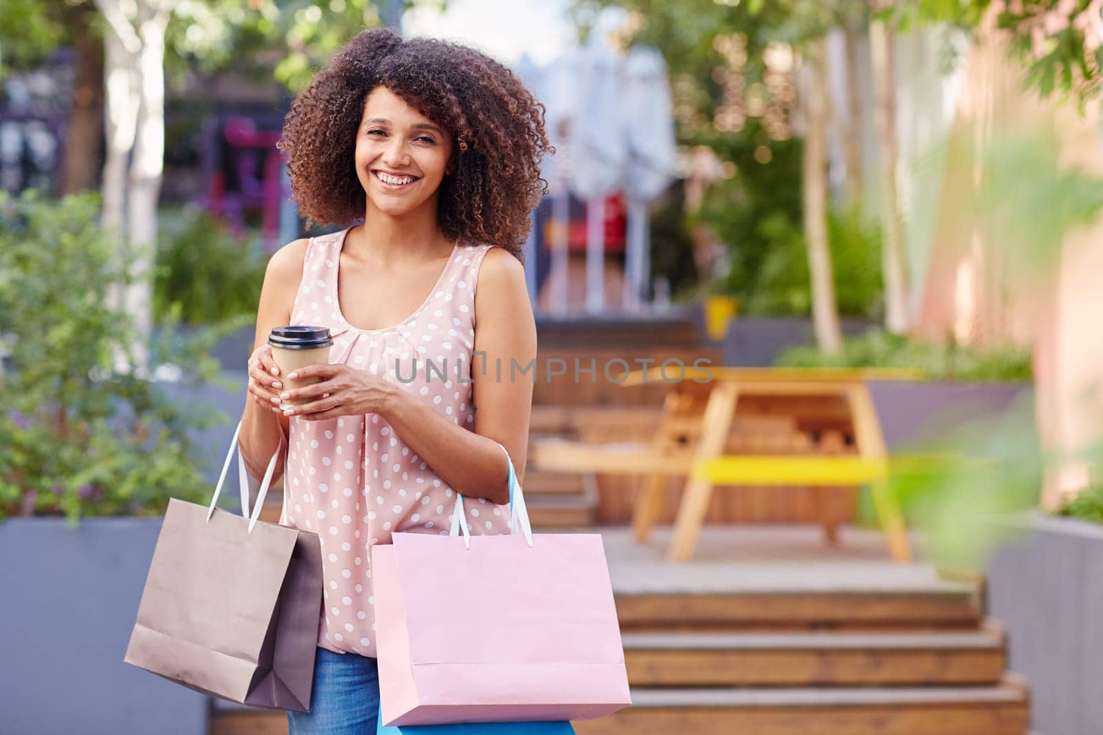 A young woman holding shopping bags and coffee outdoors