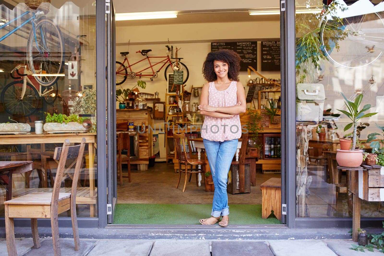 Full length shot of a young mixed race woman happily standing in the doorway of her trendy coffee shop
