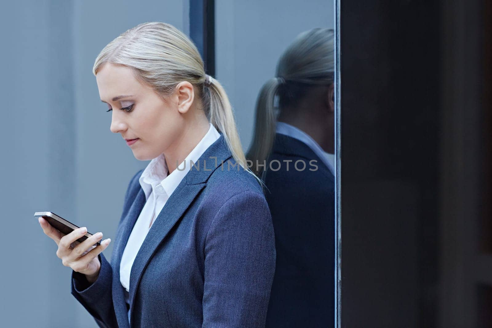 A young businesswoman typing an sms on phone with glass behind her