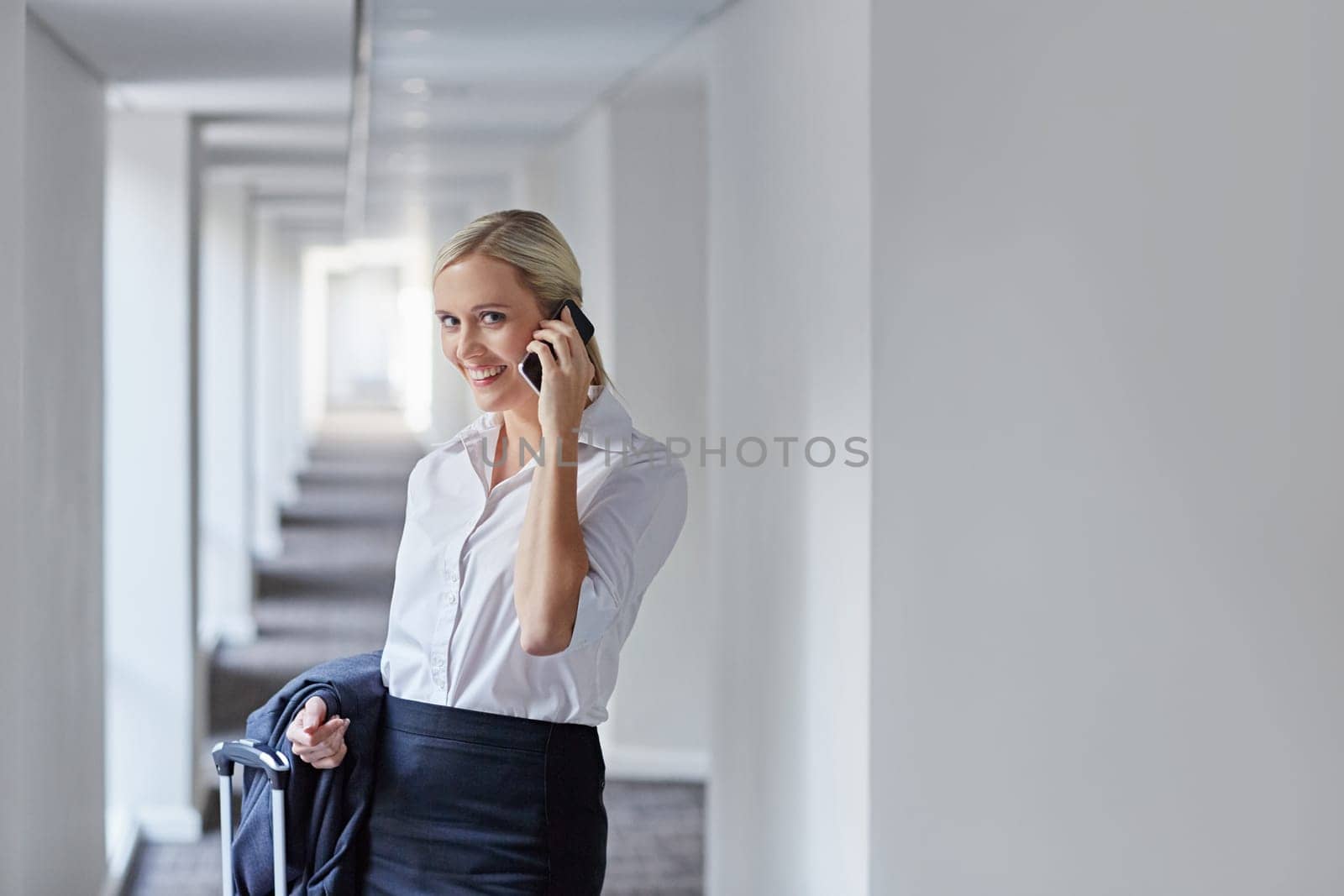 A young businesswoman with her luggage talikng on the mobile phone in a long hallway