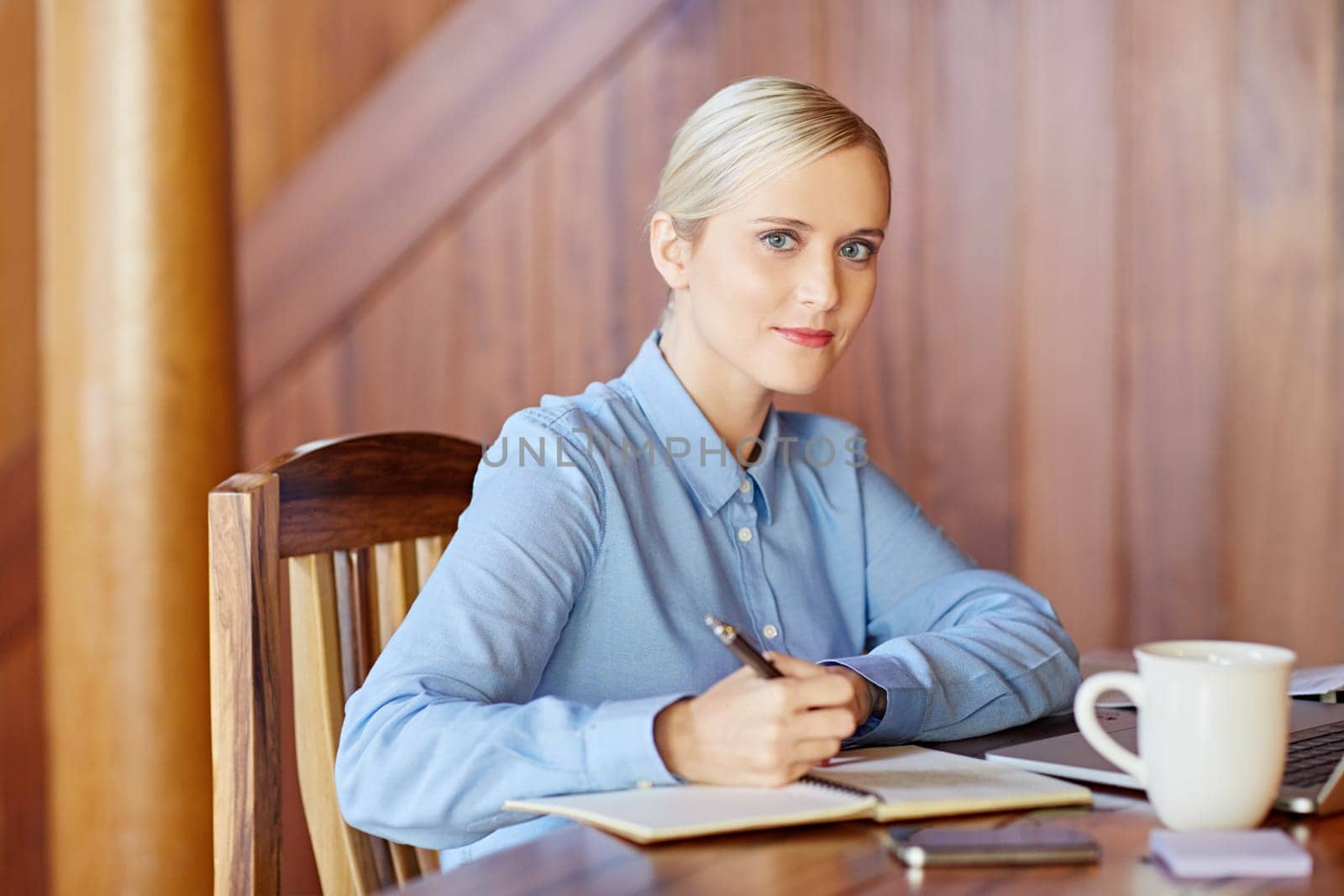 A young businesswoman taking notes in wooden office, looking in to the camera
