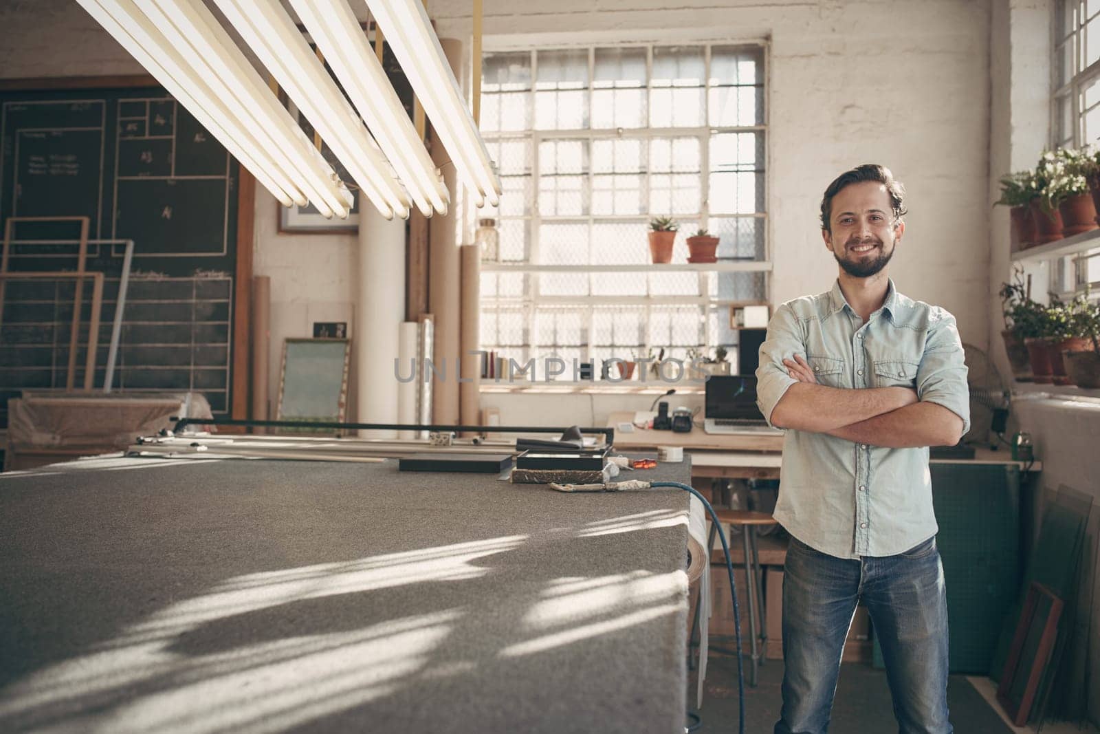 Portrait of a good looking male designer standing in his workshop studio with his arms folded and smiling confidently at the camera