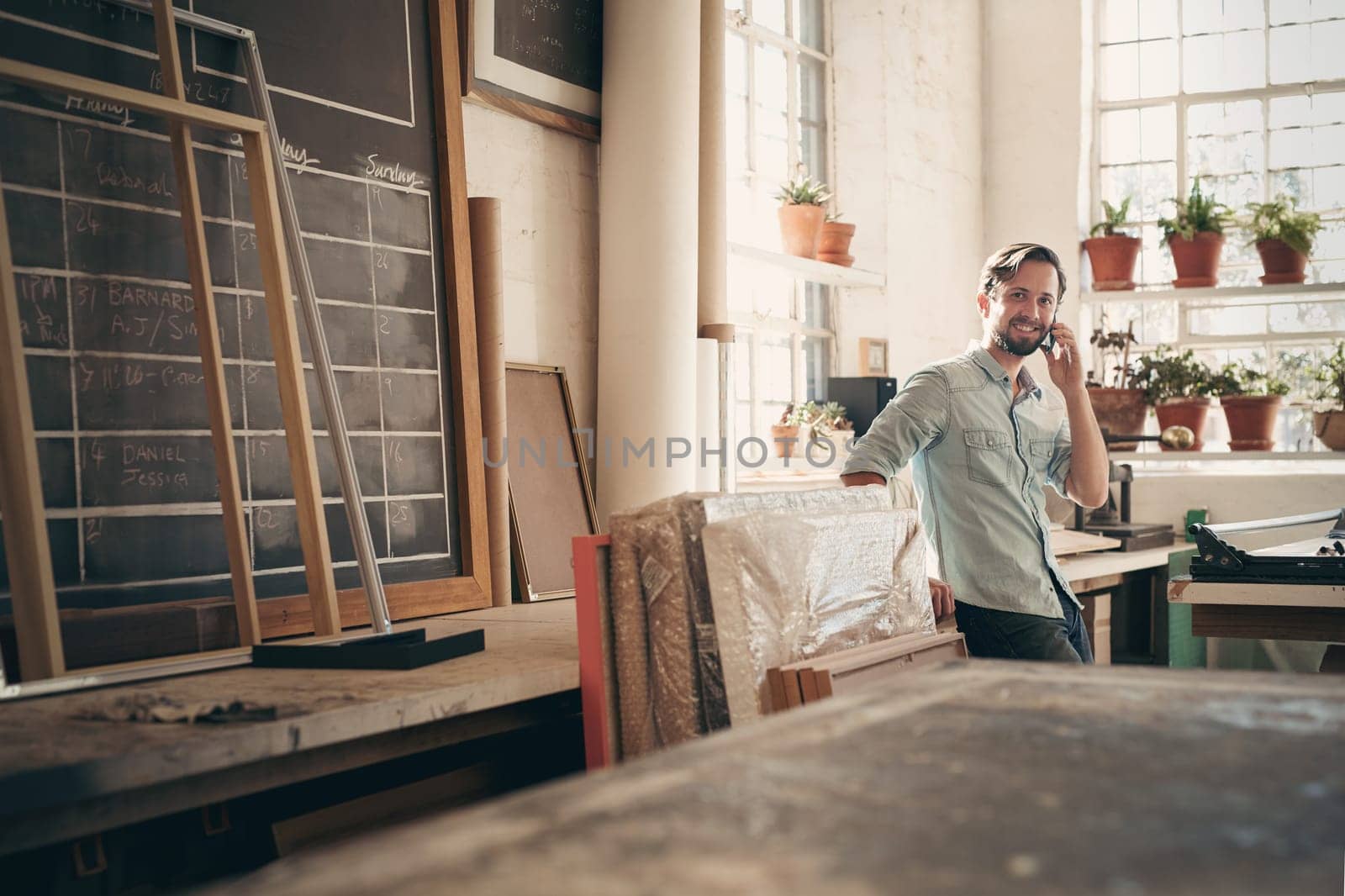 Small business owner talking on his phone while smiling and standing casually in his studio workshop