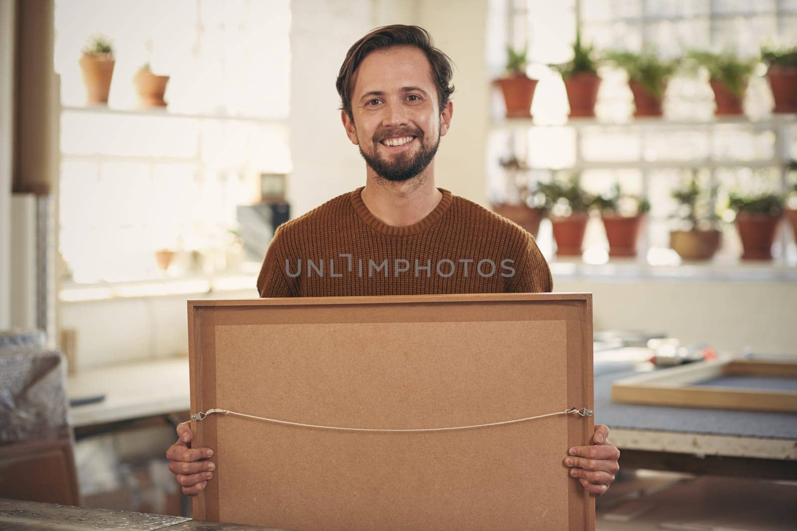 Professional framer standing in his workshop with a newly framed item and smiling at the camera