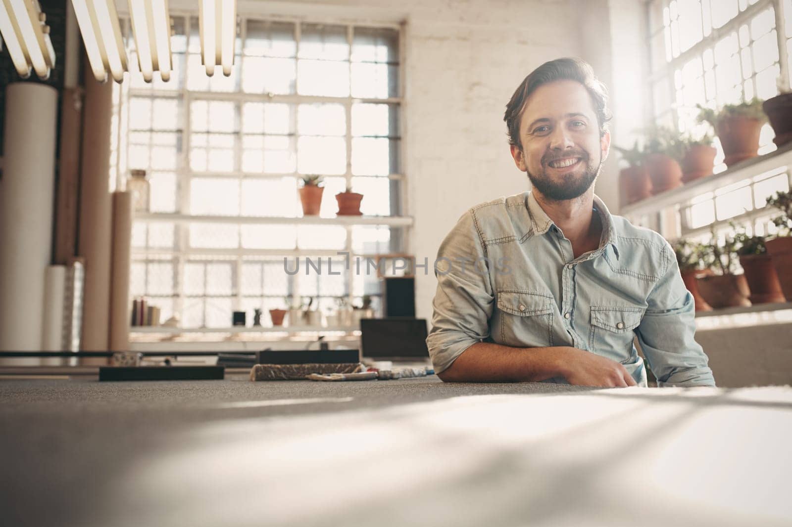 Handsome designer entrepeneur smiling at the camera while relaxing in his studio with gentle sunflare coming in through the window