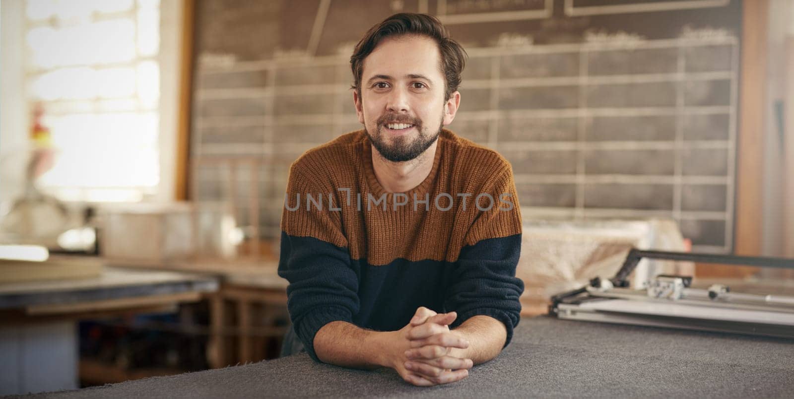 Young male designer with a positive expression leaning casually on a work area in his studio