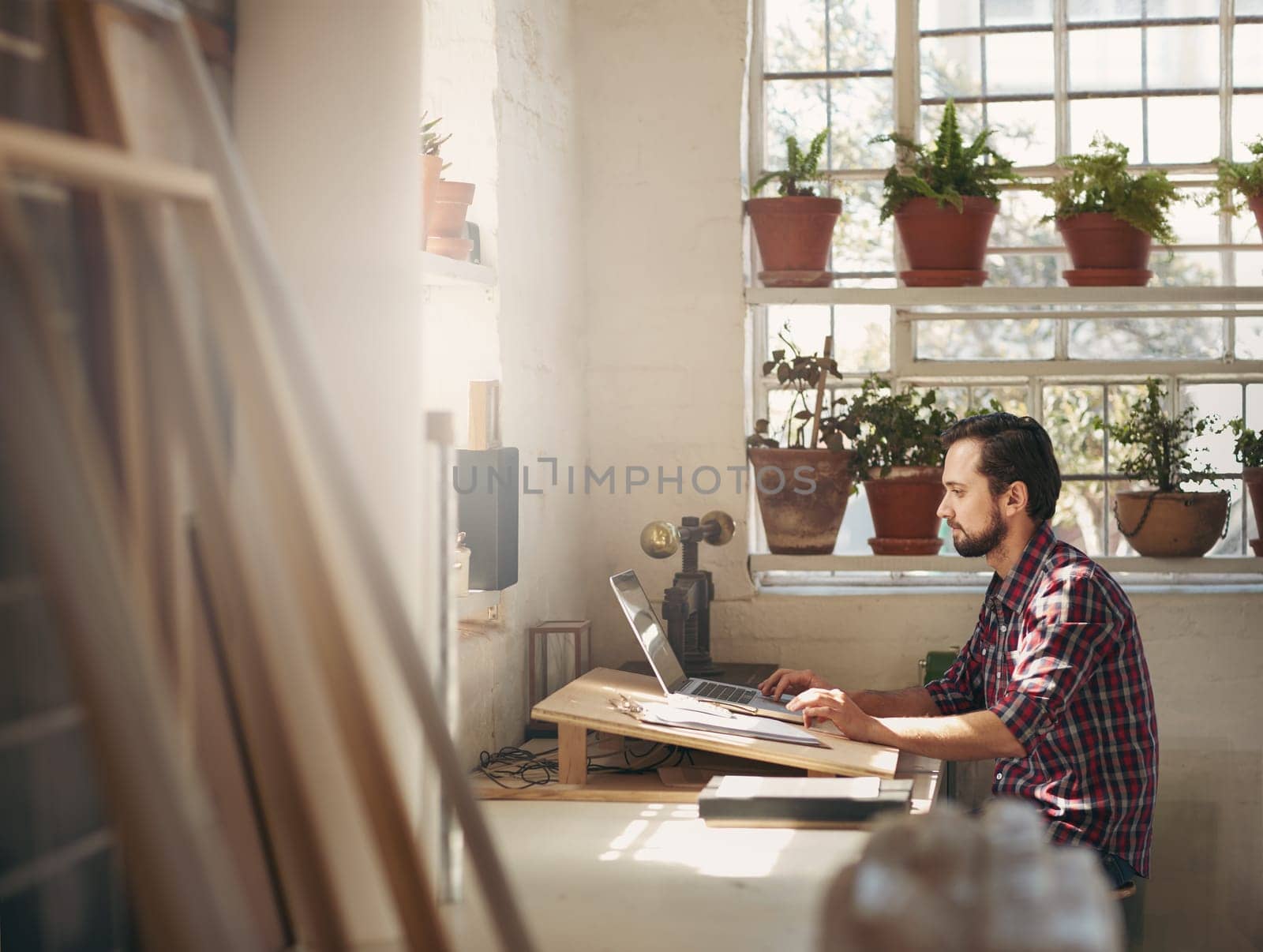 Young male designer sitting and working on his laptop in an office space in his creative design studio
