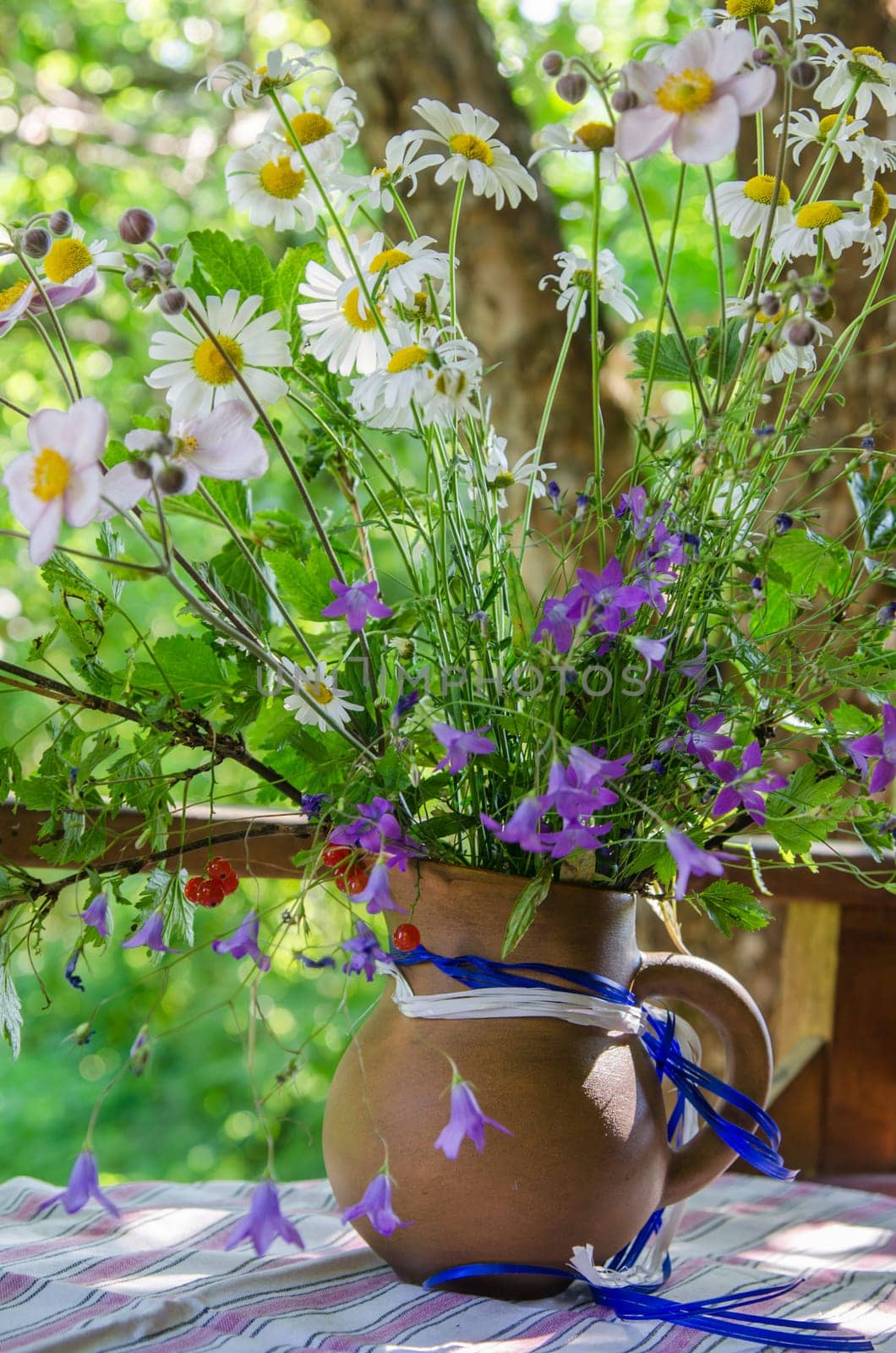 Jug with a bouquet of summer flowers on a table in the garden, close up