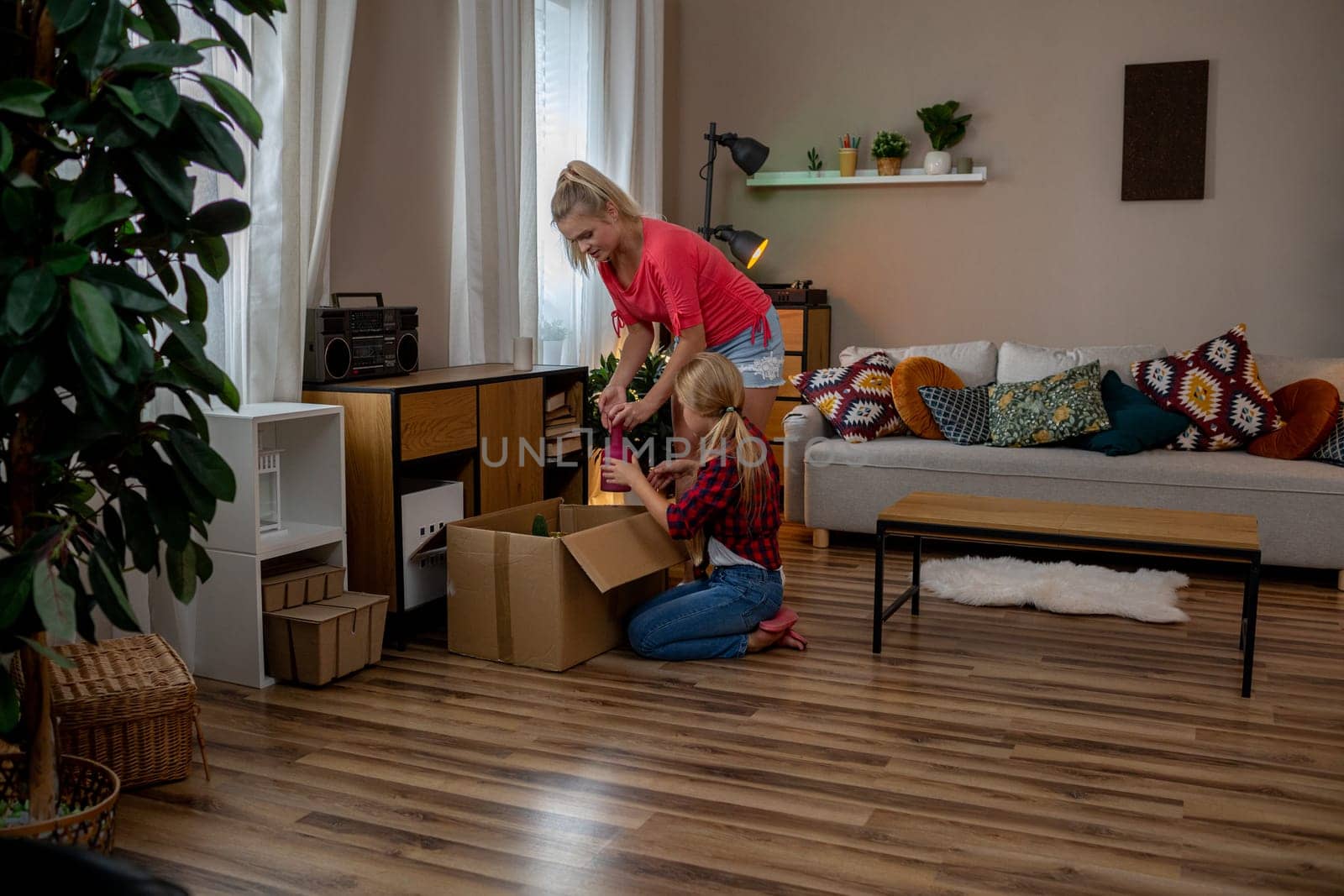 In a beautifully designed and cozy living room, a mother and her daughter find joy in unpacking boxes together