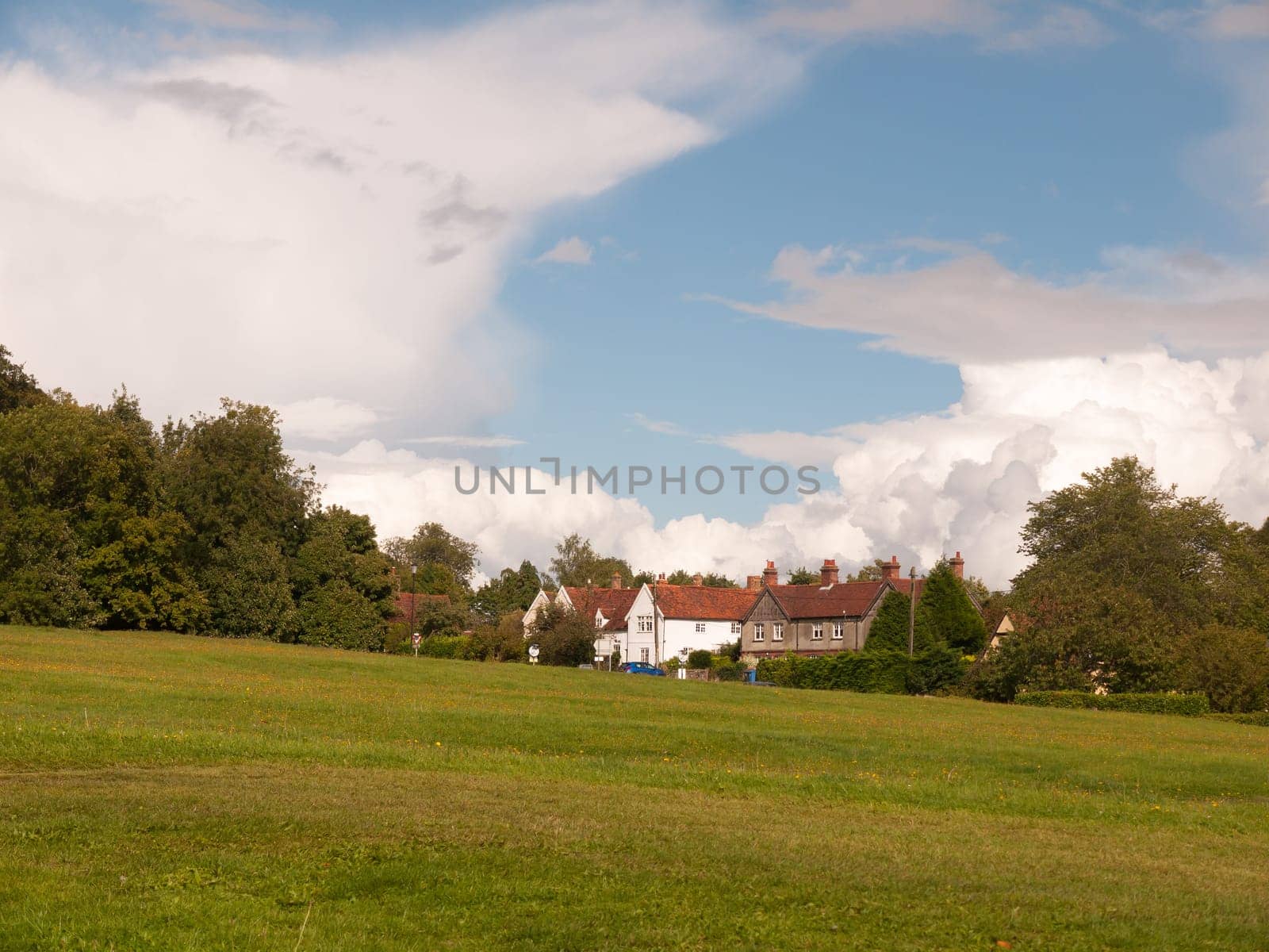 interesting sloped green lawn with country houses in background and blue and white cloud sky  England  UK
