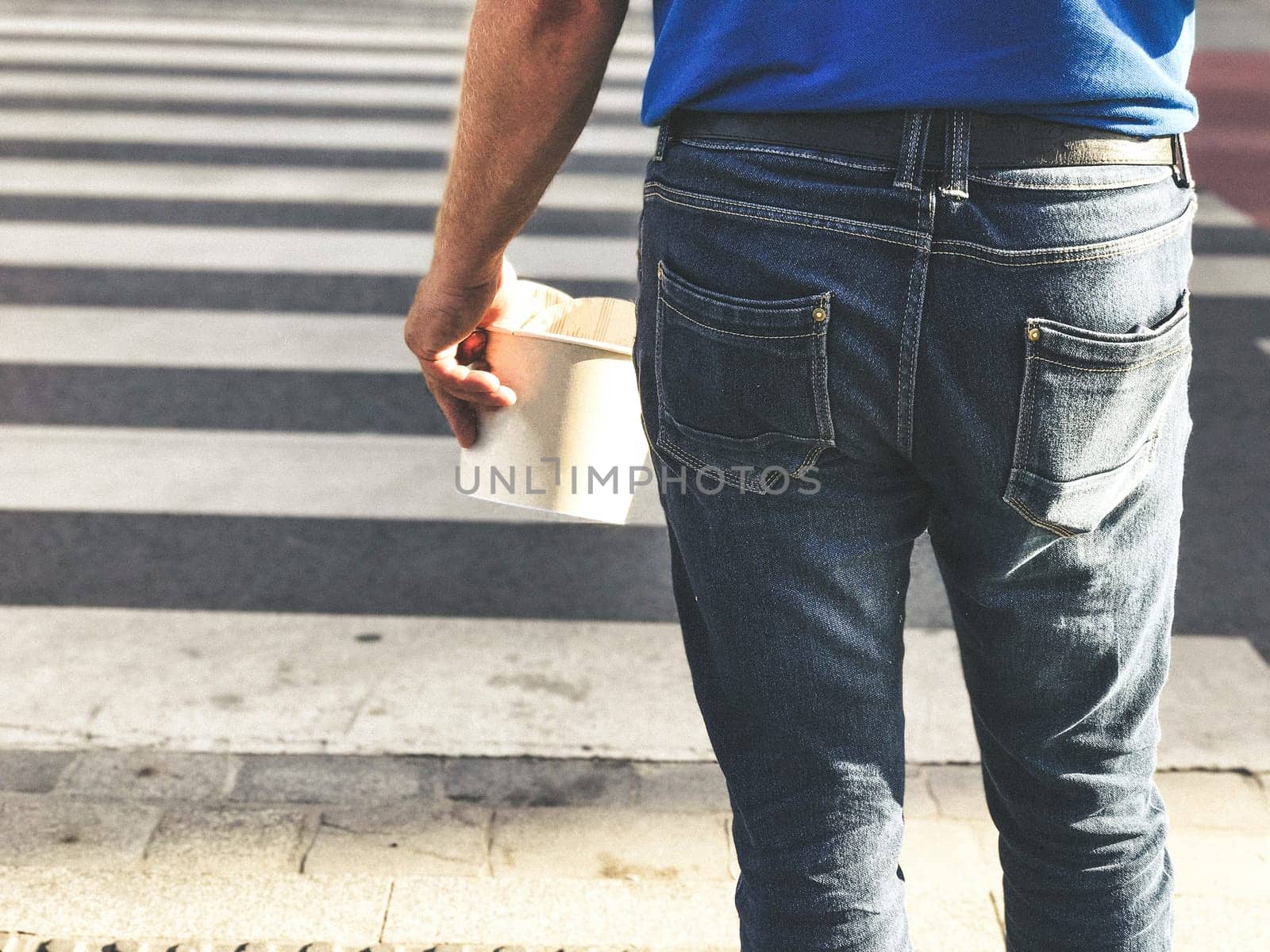 A man holds fast food in his hand and crosses the street