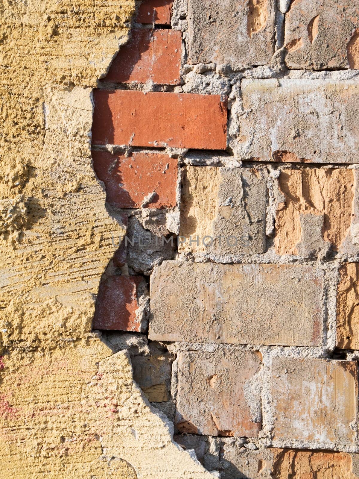 Format-filling view of old masonry with partially detached rough plaster and clinker bricks.