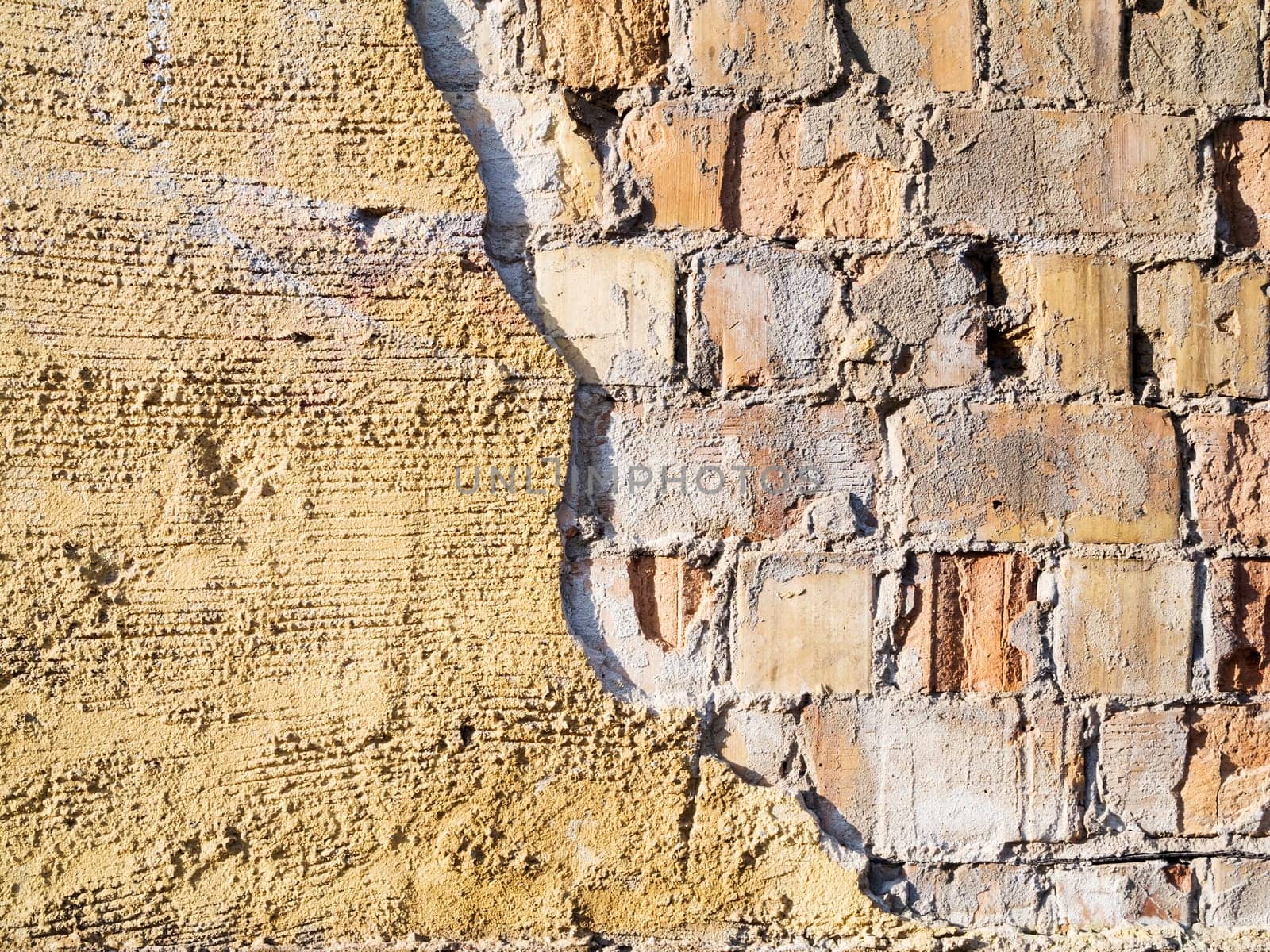 Format-filling view of old masonry with partially detached rough plaster and clinker bricks.