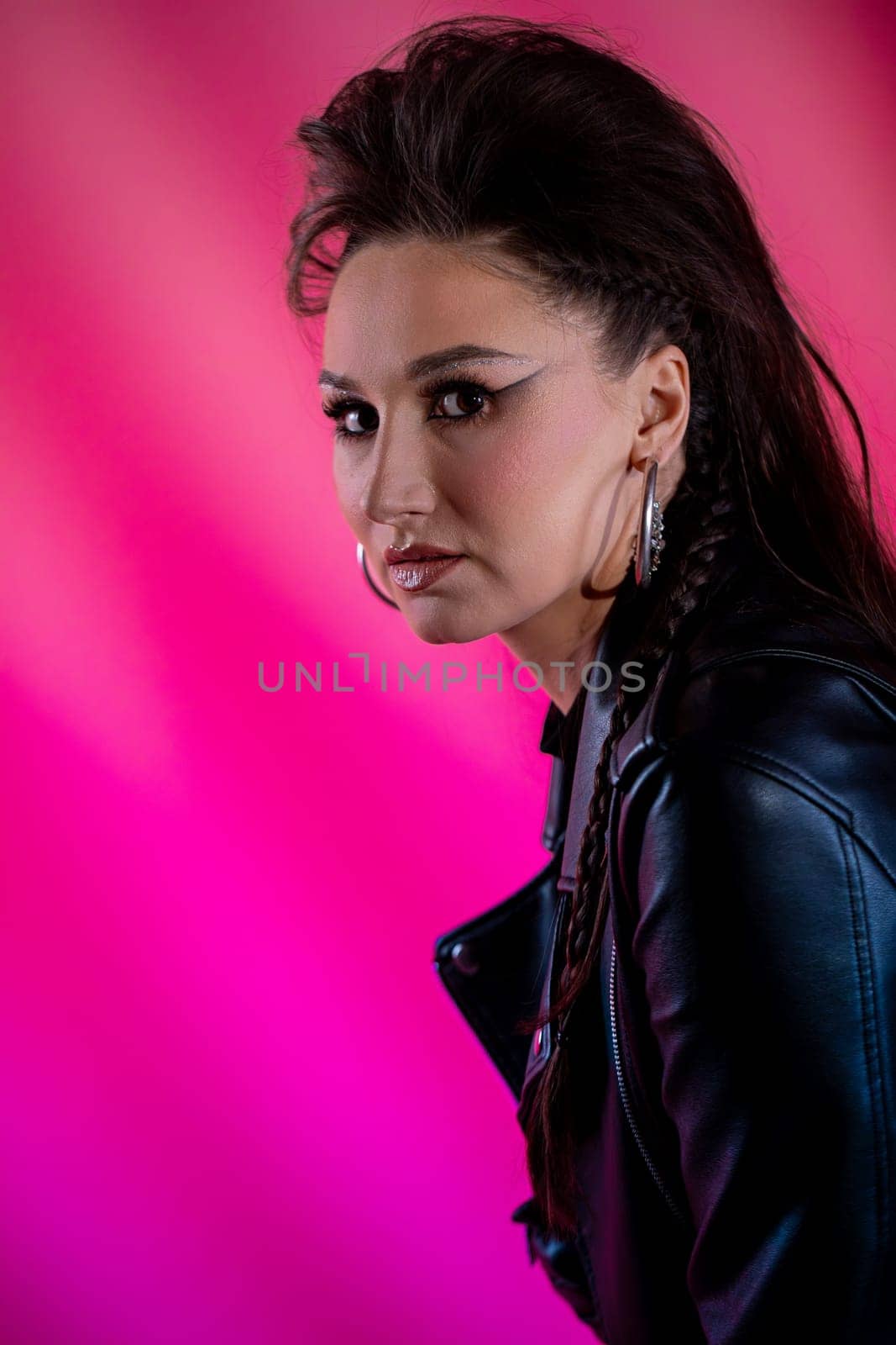 A striking and bold portrait of a confident woman wearing a stylish leather jacket against a vibrant pink backdrop