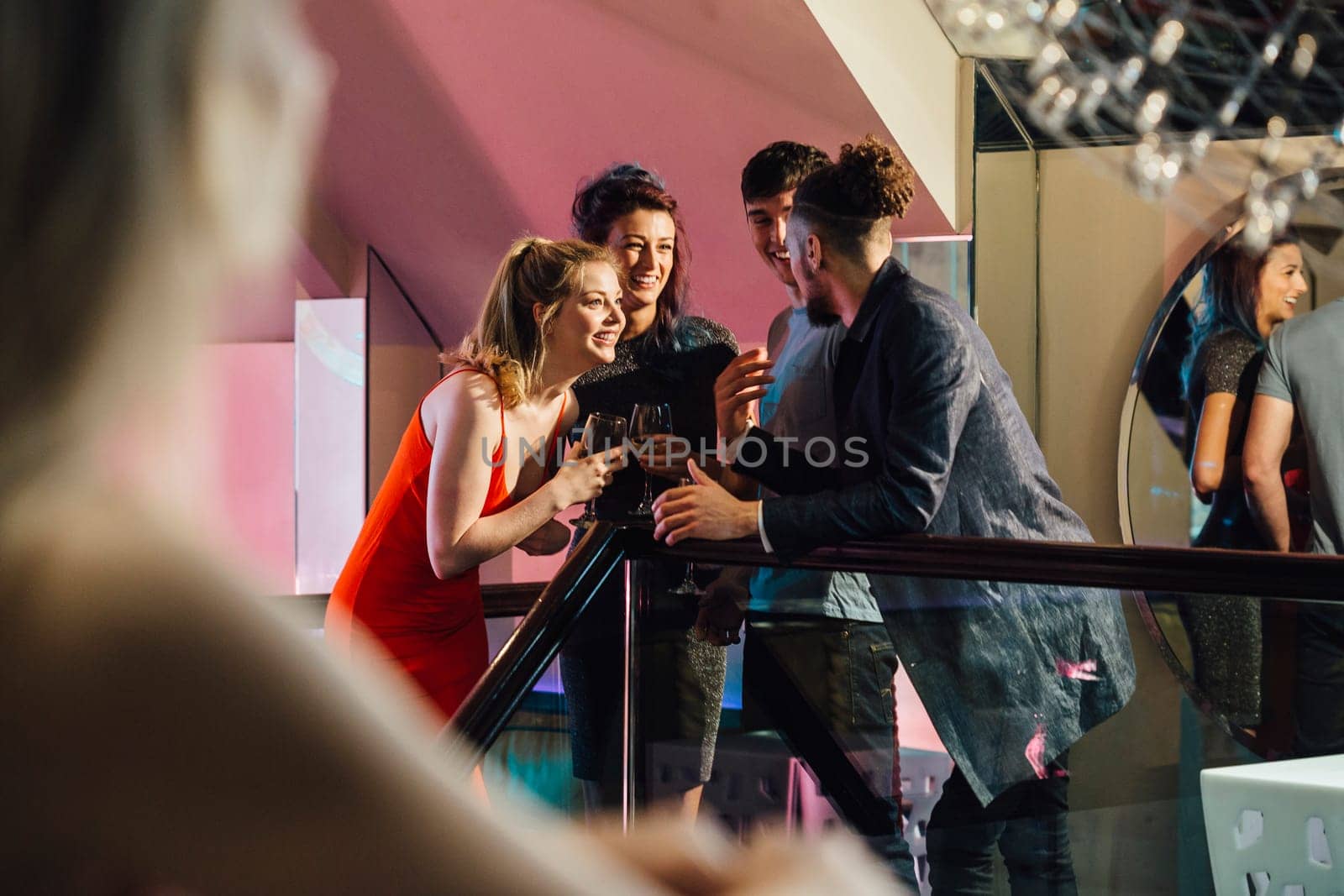 Friends are standing in a nightclub together drinkiong cocktails while they chat.