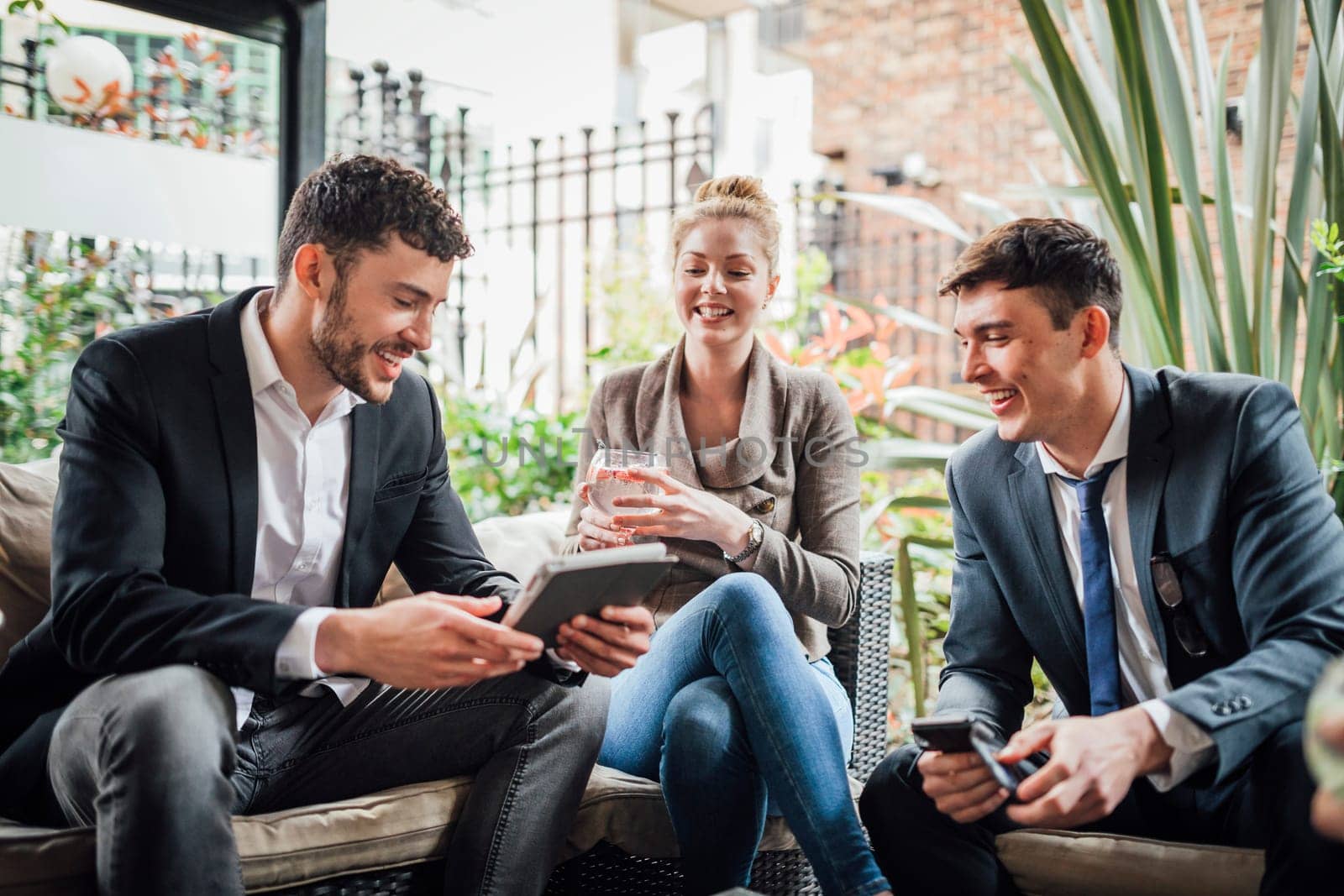 Business people are discussing work on a digital tablet while enjoying drinks in a bar courtyard.