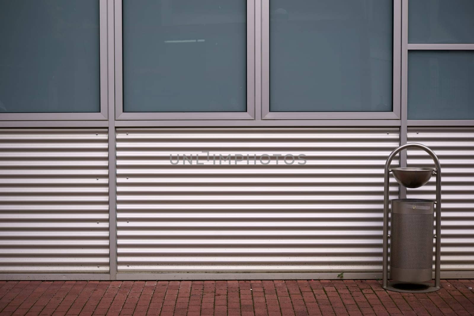The sheet metal cladding of a modern building in front of which stands a trash can.