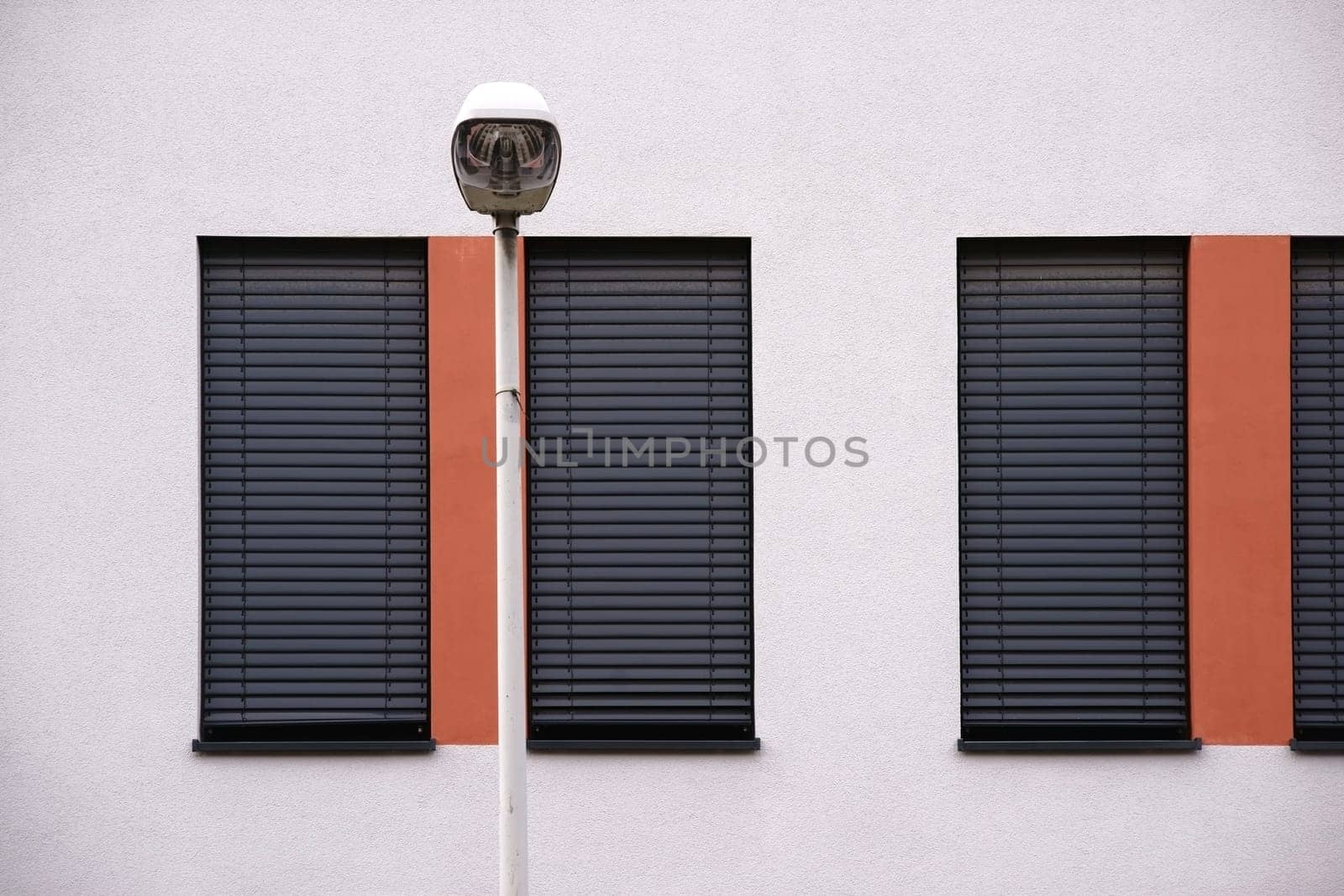 The modern façade of a modern residential building with windows with metal blinds and street lighting.