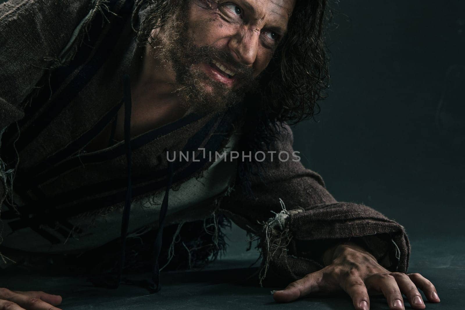 Actor in makeup, a poor man on black studio background. The bum in canvas rags. Concept of vagrancy and survival. Concept of pain and suffering. The wounded man crawling to salvation