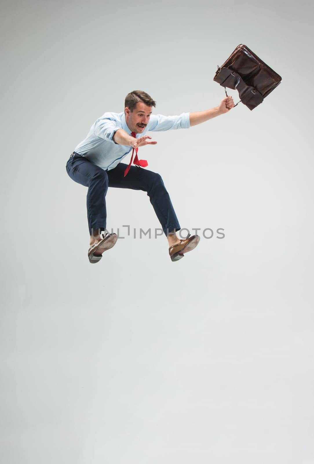 Businessman running or jumping with a briefcase, isolated on gray studio background