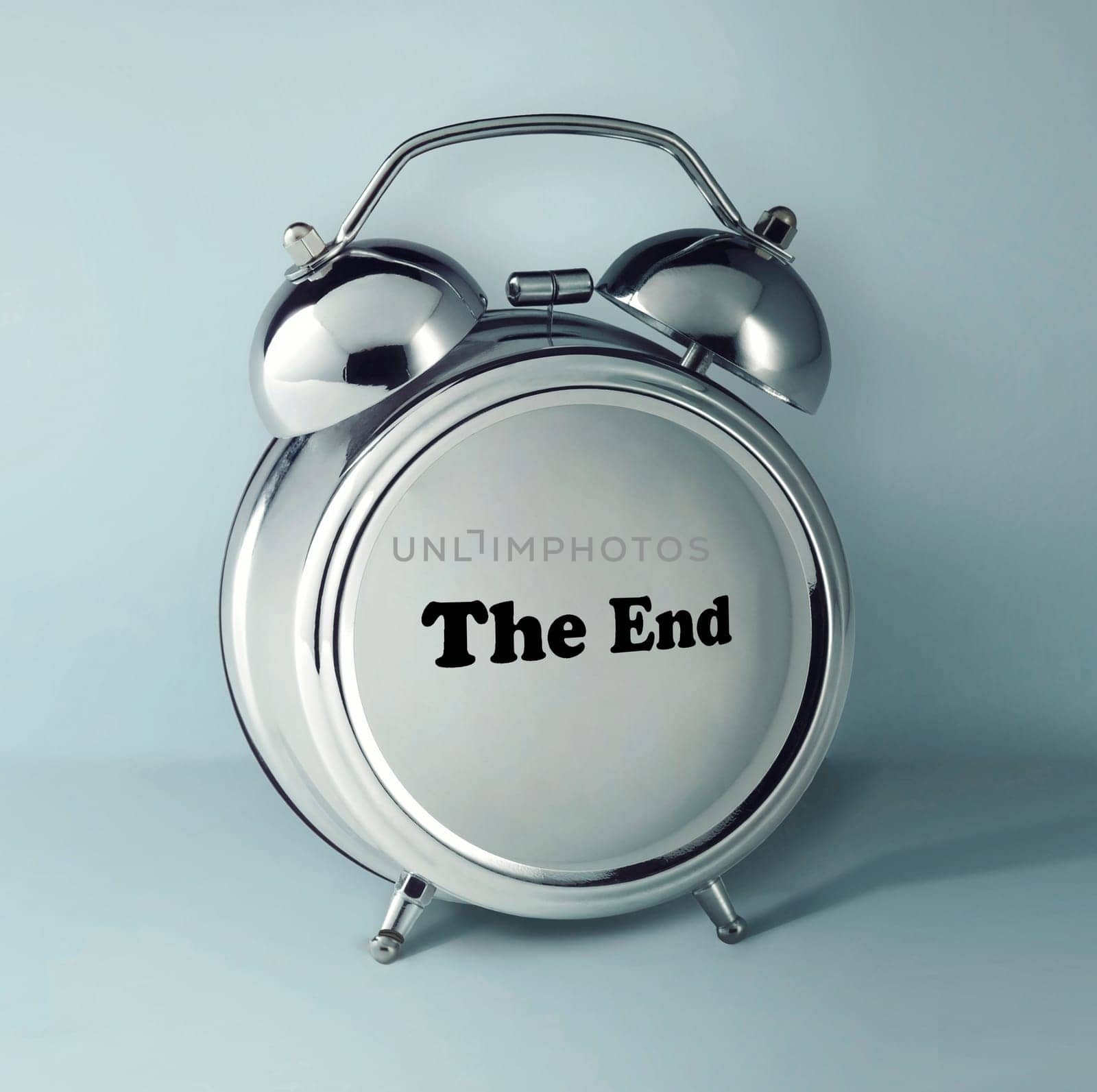 The conceptual image of alarm clock with word THE END on empty clock face against gray studio background. concept of the end of the process