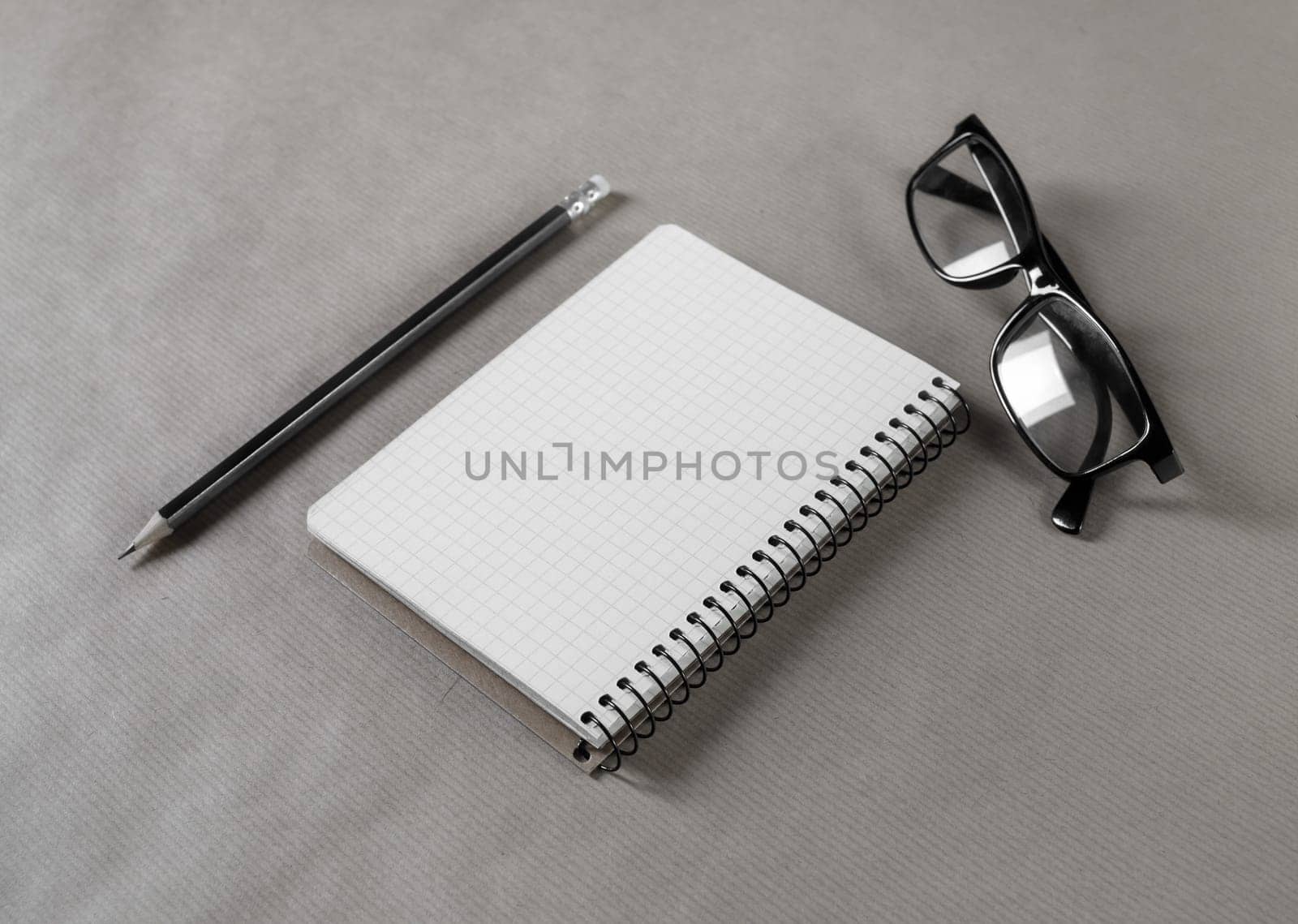 Blank notepad, glasses and pencil on craft paper background. Stationery elements. Responsive design mockup.