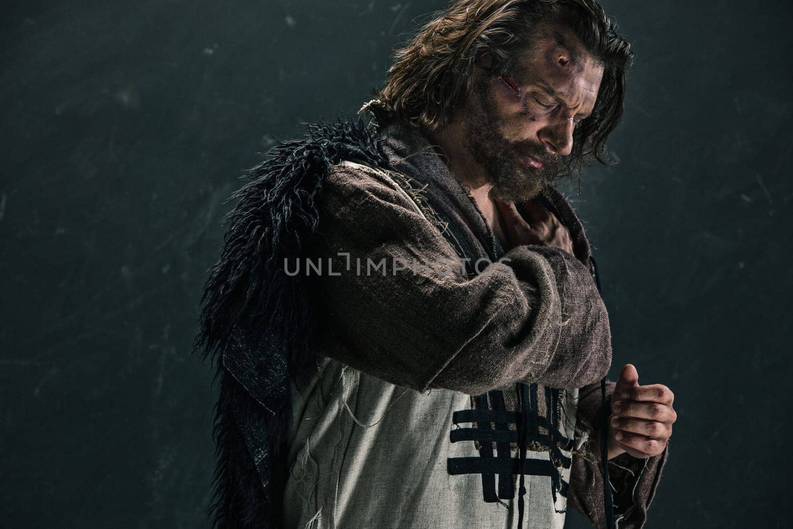 Actor in makeup, a poor man on black studio background. The bum in canvas rags. concept of vagrancy and survival. concept of pain and suffering